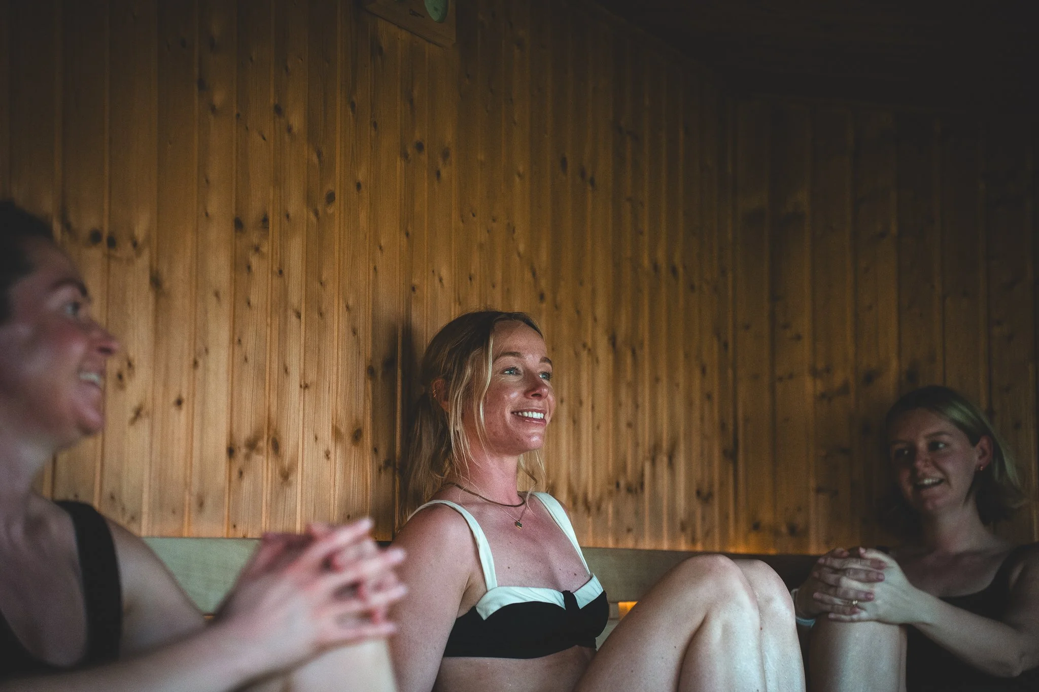 At Unfold Sauna Club Three women sitting in a wooden sauna with relaxed and happy expressions.