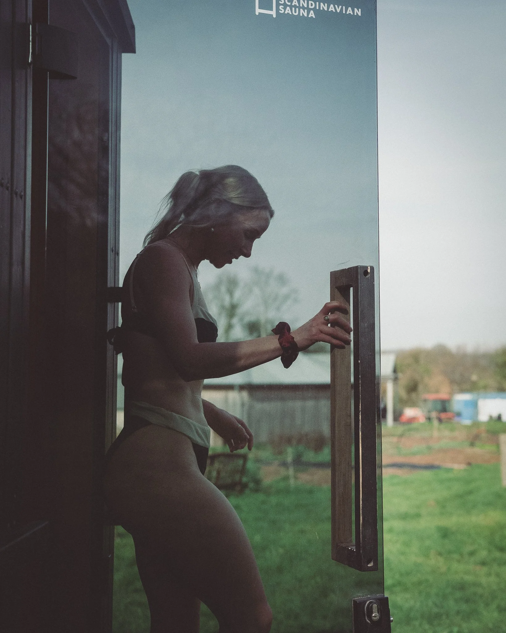 At Unfold Sauna Club A woman in athletic wear entering a Scandinavian sauna through a glass door.