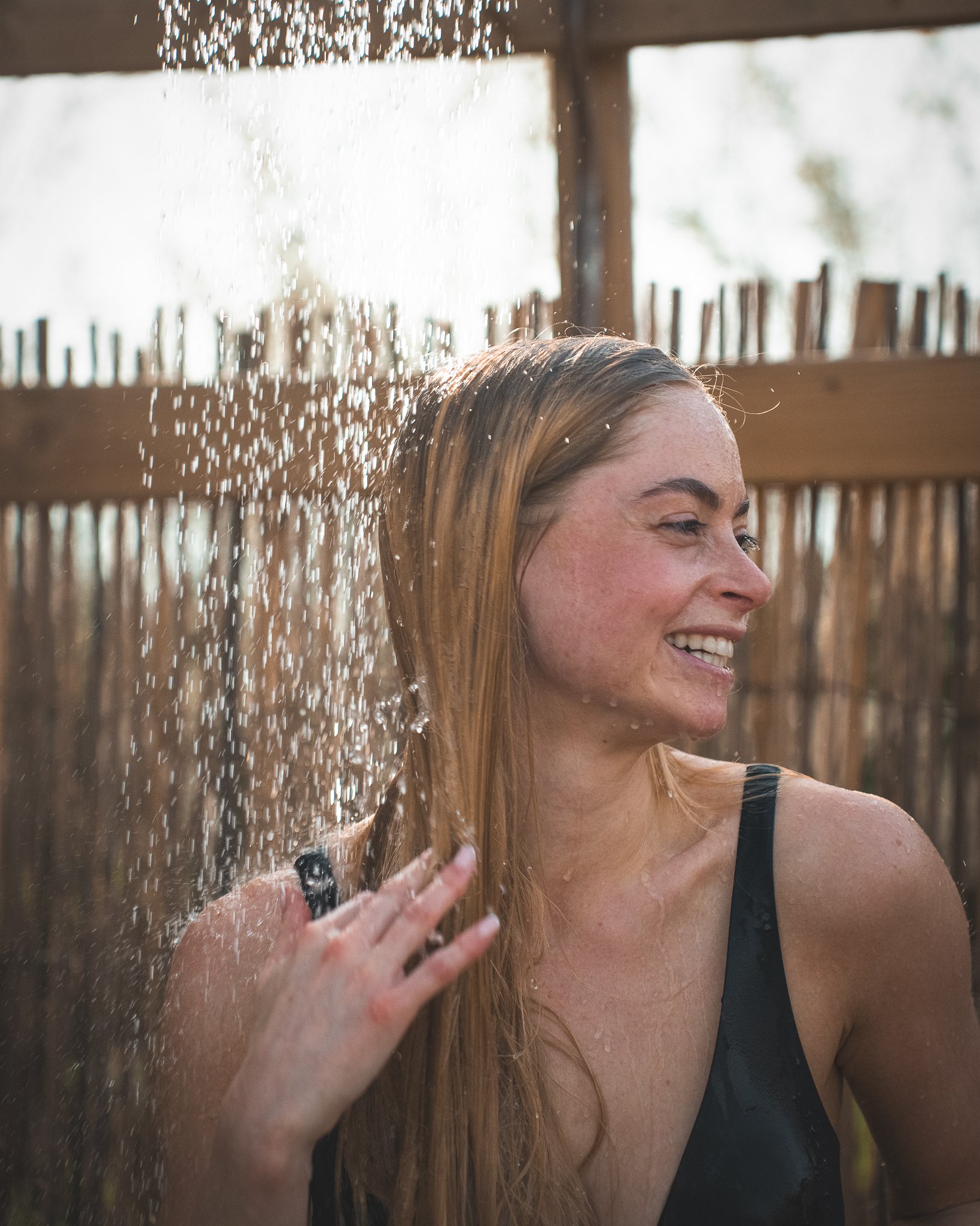 At Unfold Sauna Club A woman enjoying an outdoor shower, smiling while water sprays over her head.