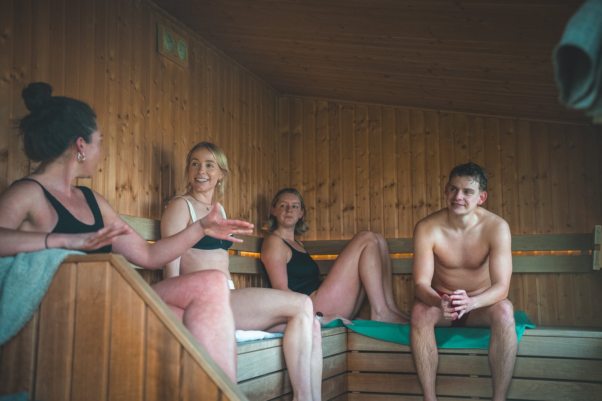At Unfold Sauna ClubFour young adults sitting inside a wooden sauna, engaging in conversation and smiling.