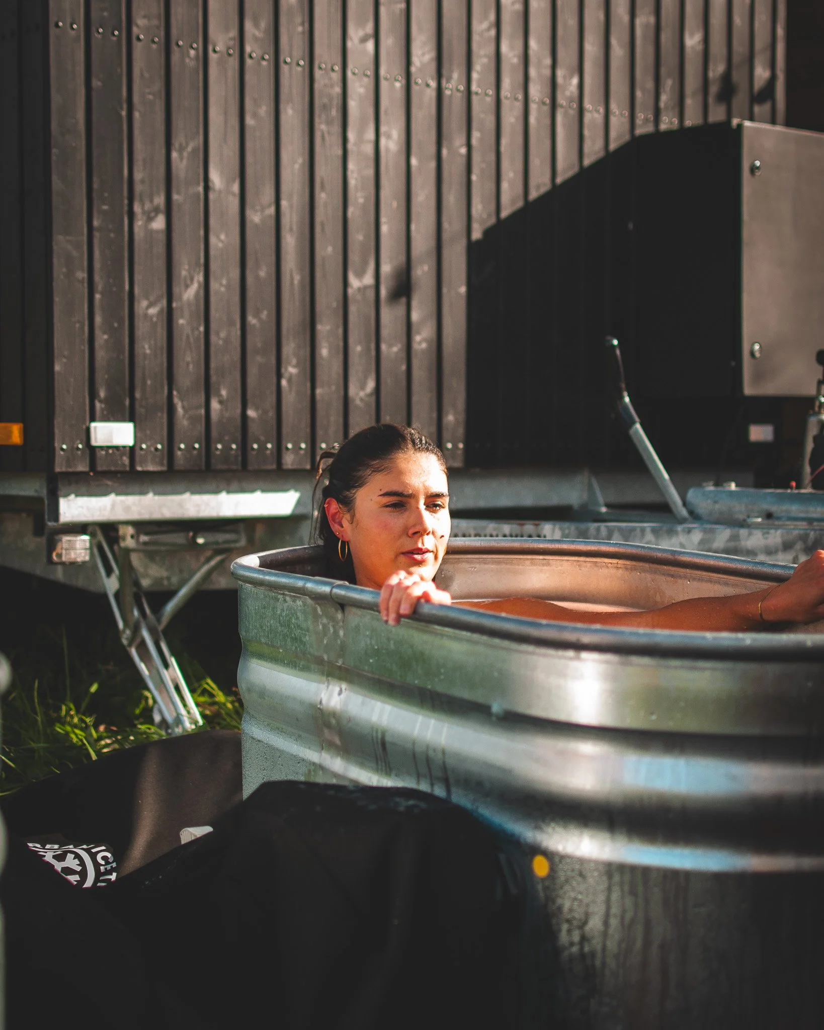 At Unfold Sauna ClubA woman with dark hair in a ponytail relaxing in an outdoor hot tub, with a wooden structure behind her.
