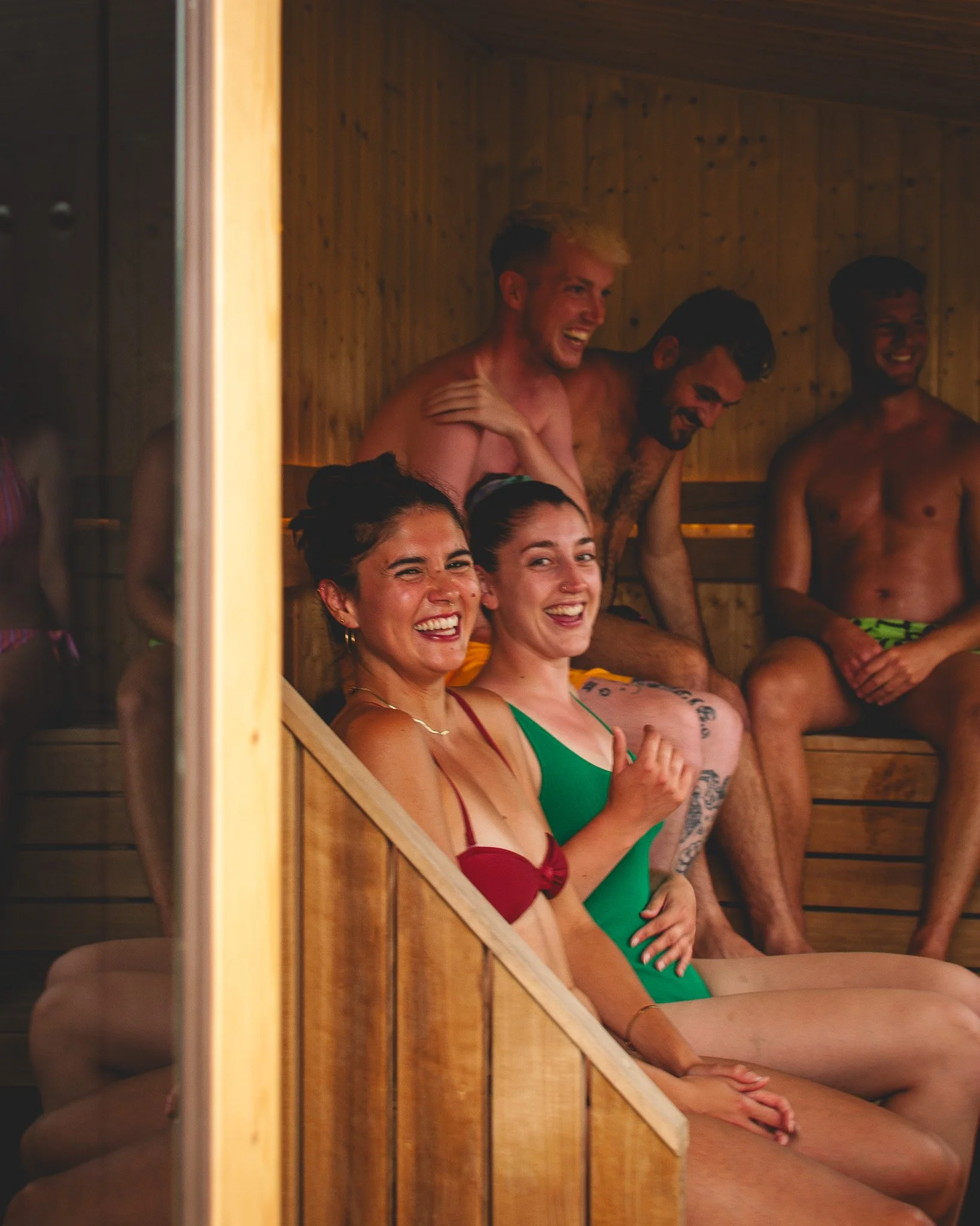 At Unfold Sauna Club People laughing and enjoying a sauna, seated on wooden benches inside a wooden room.