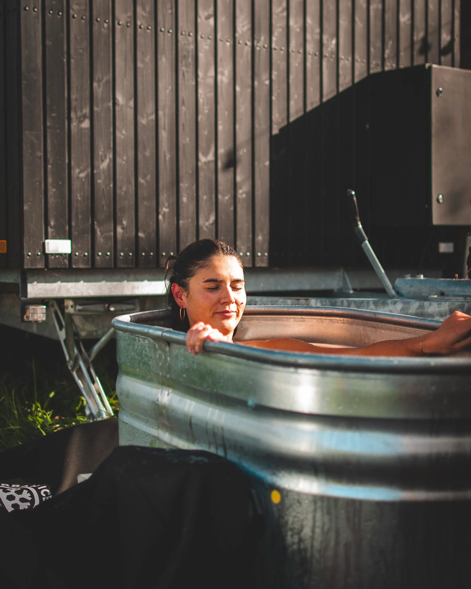 At Unfold Sauna Club Woman relaxing in an outdoor metal tub with a wooden wall in the background.
