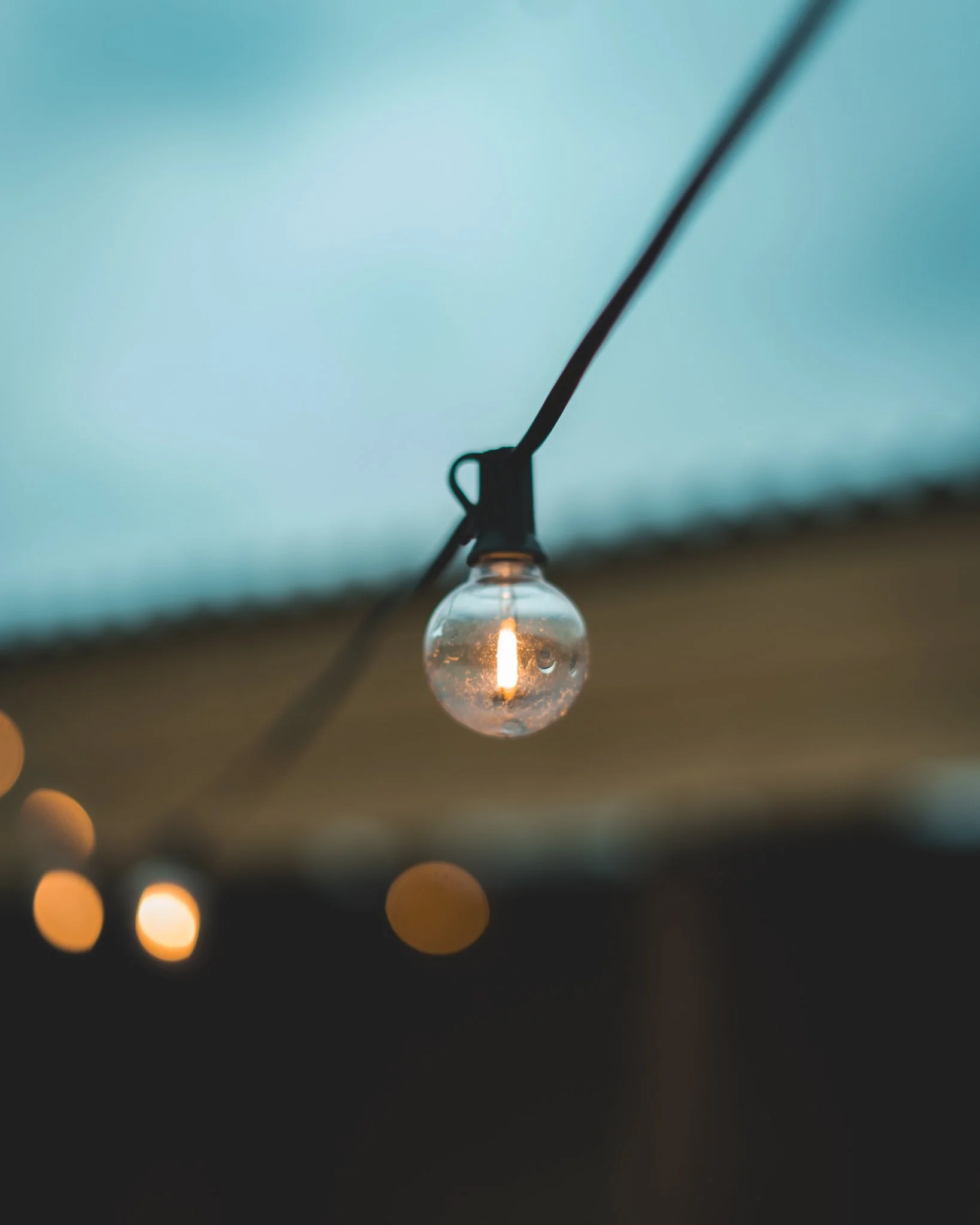 At Unfold Sauna Club String of outdoor string lights with one clear bulb lit, blurred background of evening sky.