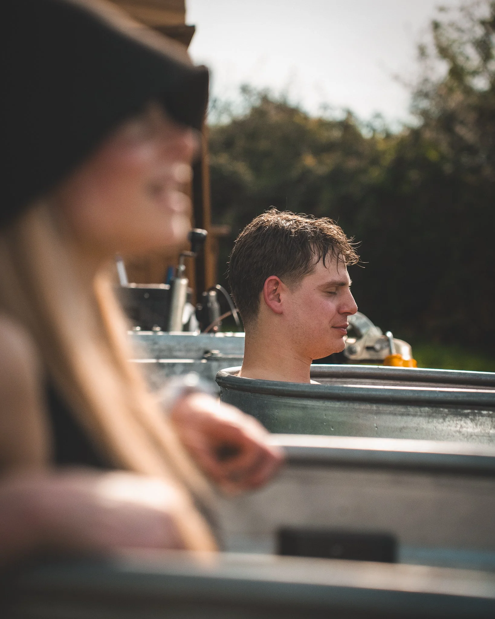 At Unfold Sauna Club A young man with closed eyes relaxing in a boat with greenery and trees in the background.