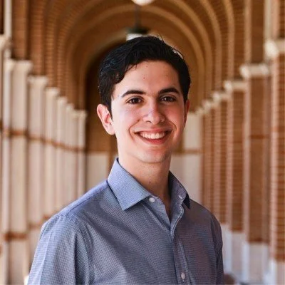 A young man smiling, standing in a corridor with brick arches.