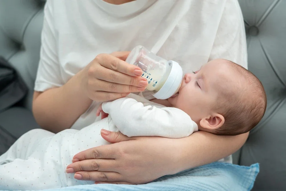 Adult feeding a baby with a bottle in a hospital setting.