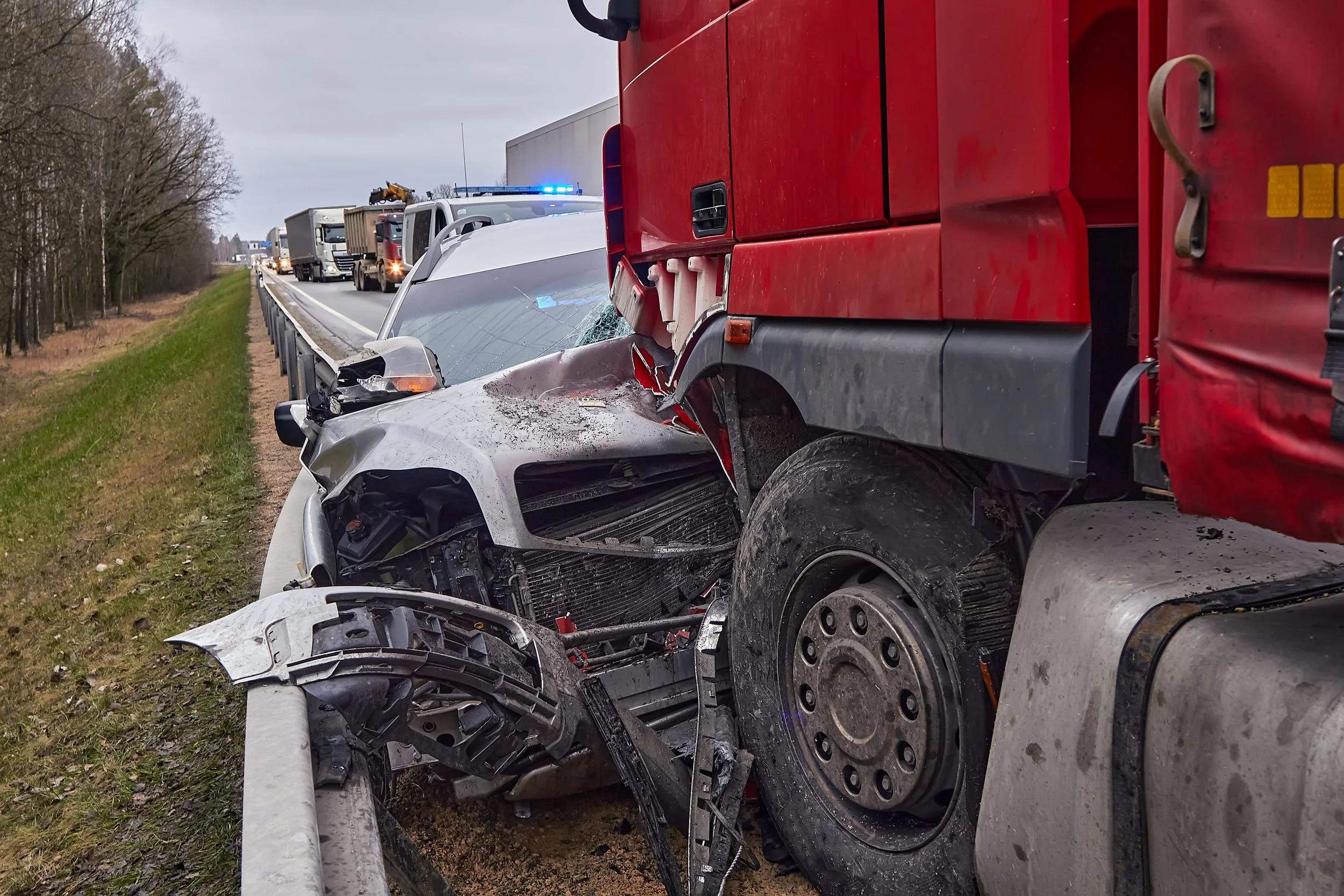 A multi-vehicle collision involving a car and a large red truck on a highway, with emergency vehicles and a line of traffic in the background.