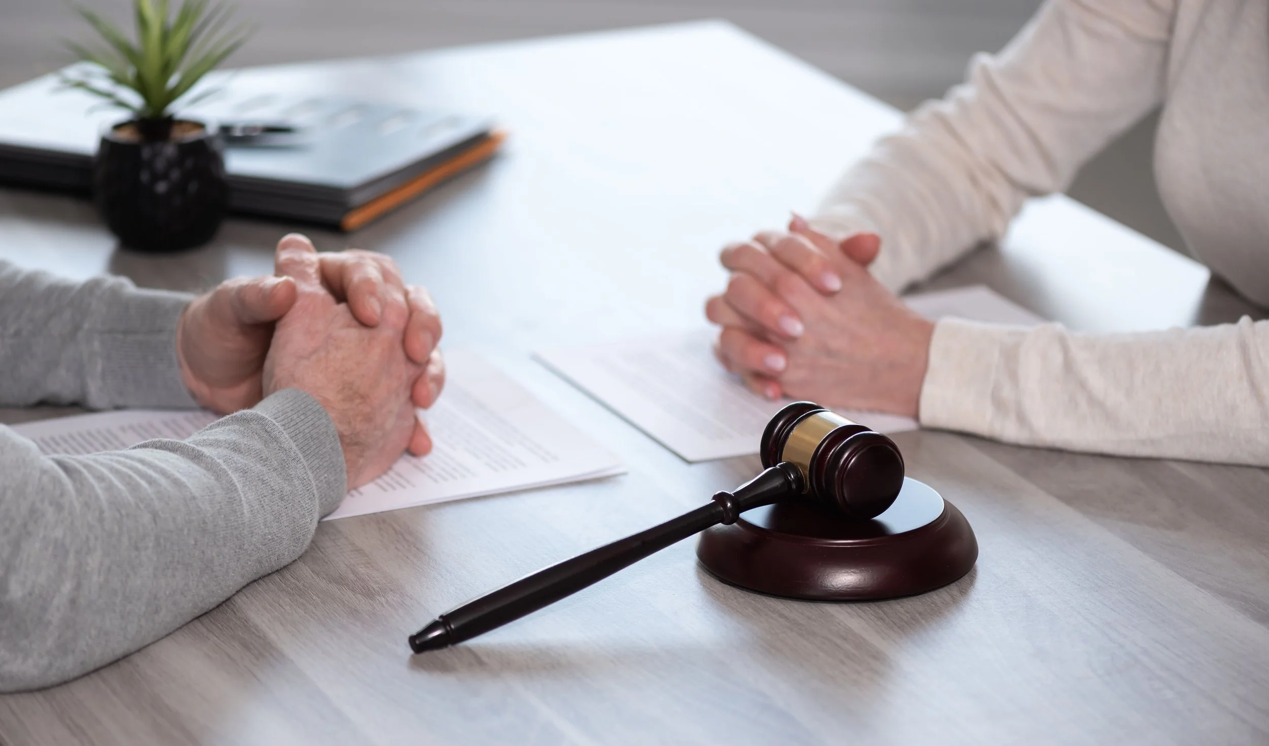 Two people with hands clasped, sitting at a table in a legal or formal setting, with a judge's gavel on the table.