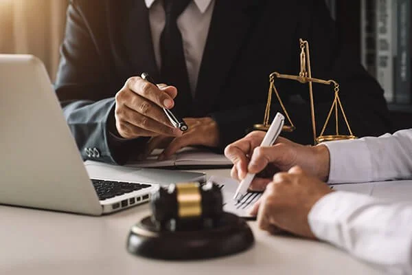 Two people in business attire sitting at a desk with a laptop, a gavel, and a scale of justice, discussing legal matters.