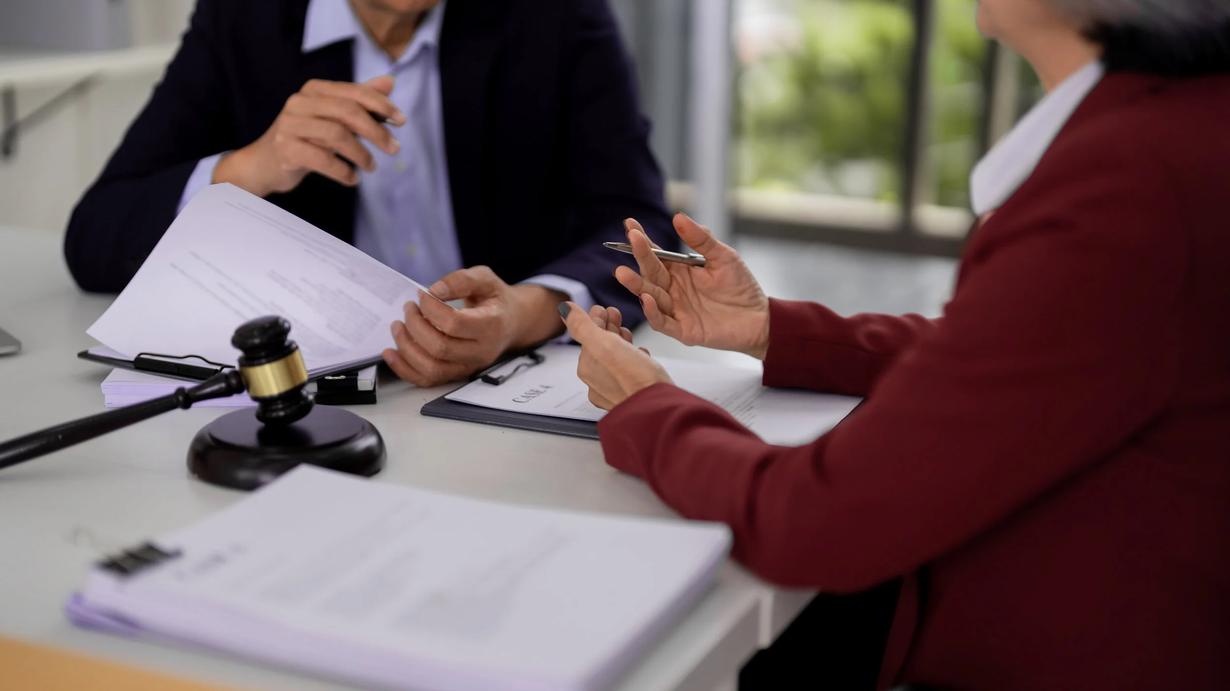 Two people having a legal or business discussion at a desk, with documents, a gavel, and a laptop.