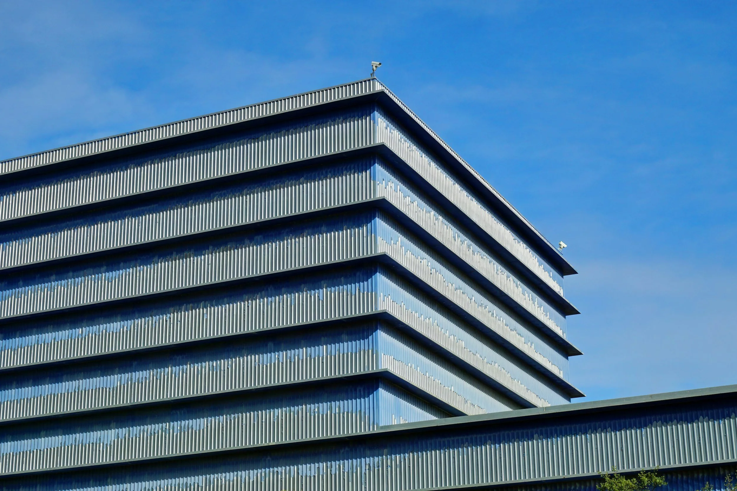 Modern multi-story building with glass and metal exterior against a blue sky.