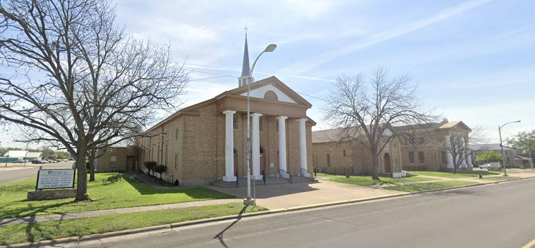 A church building with tall white columns, a pediment, and a steeple under a clear blue sky, with leafless trees and a sidewalk in the foreground.