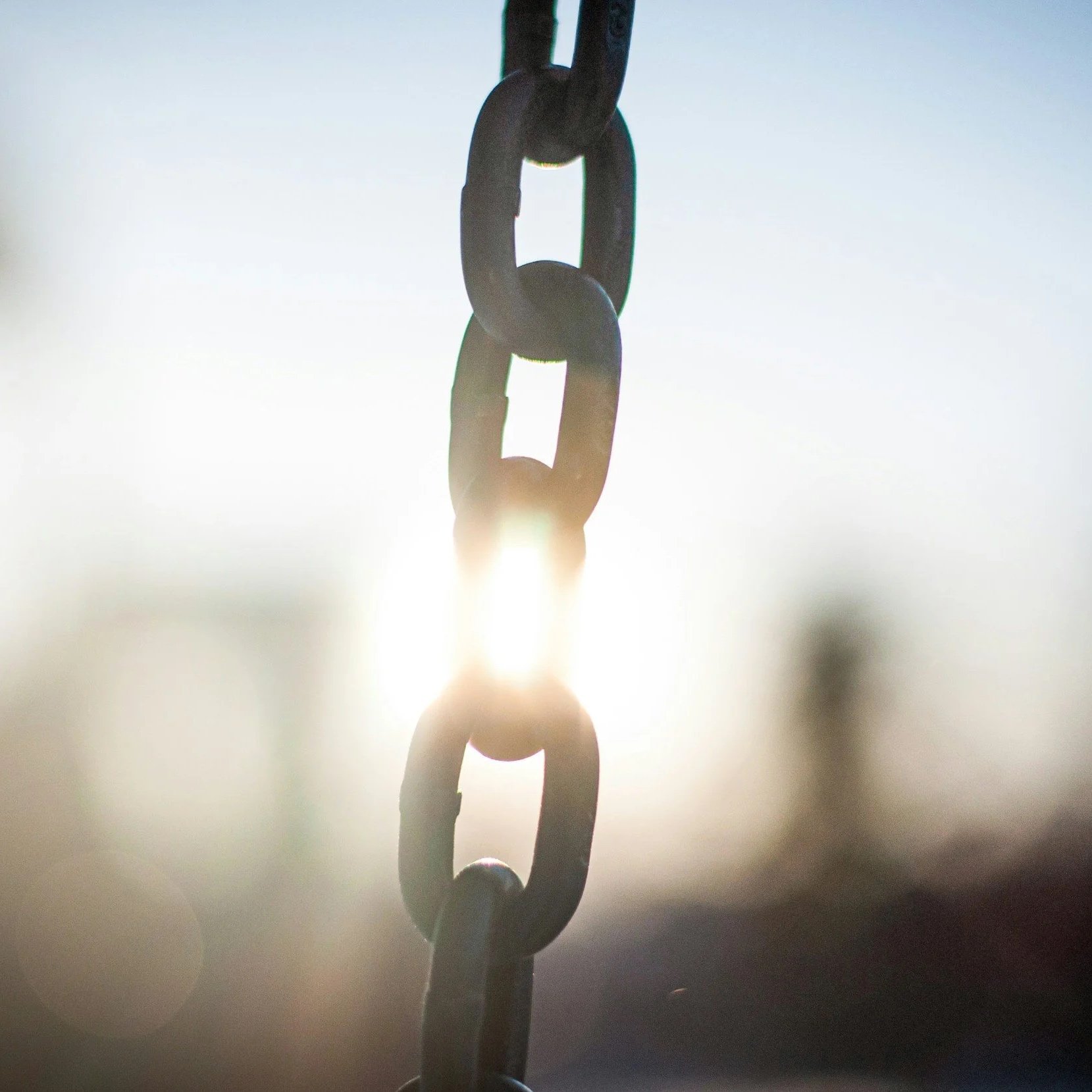 A metal chain hanging with sunlight shining through the links.