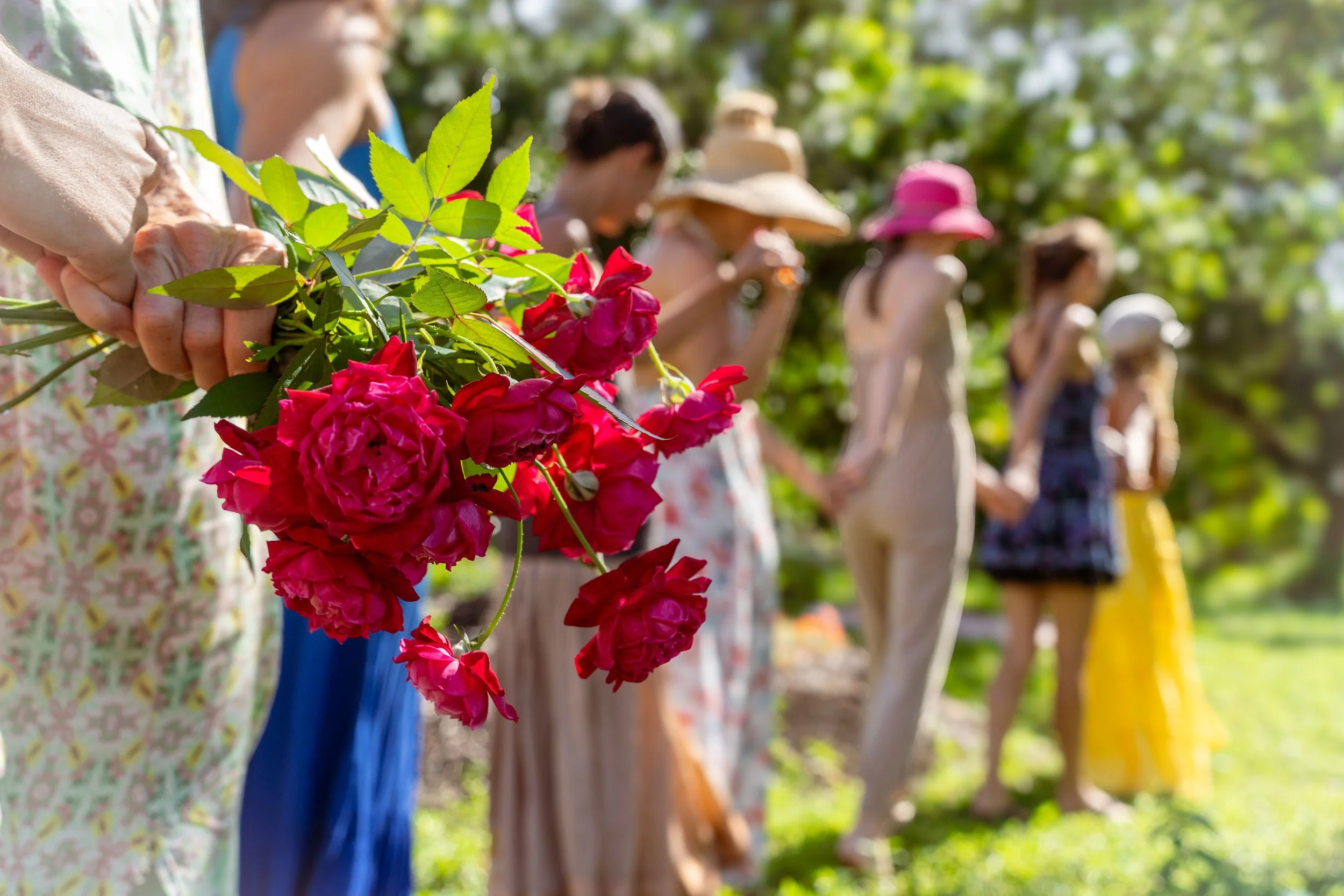 Line of women holding flowers at an outdoor event with green trees in the background.