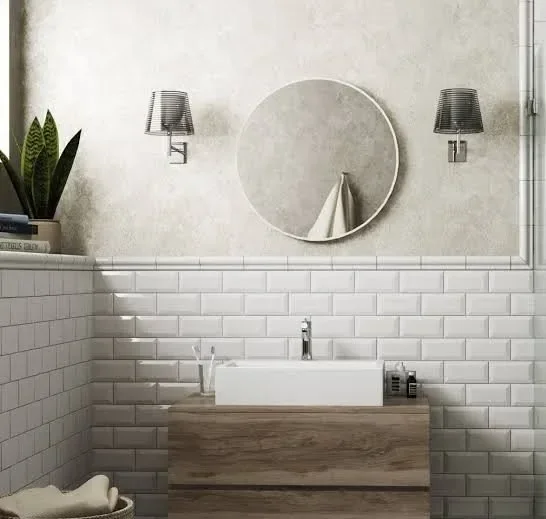 Badezimmer mit Wandspiegel, zwei Wandlampen, Waschbecken auf Holzwandkonsole, weiße Fliesen und Zimmerpflanze.