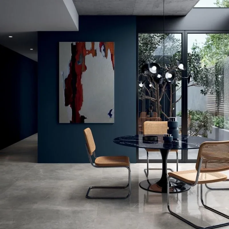 Moderne Wohnung mit einem runden schwarzen Esstisch, vier Stühlen aus Rattan mit Metallrahmen, Wandkunst und großen Fenstern mit Blick auf einen Garten.
