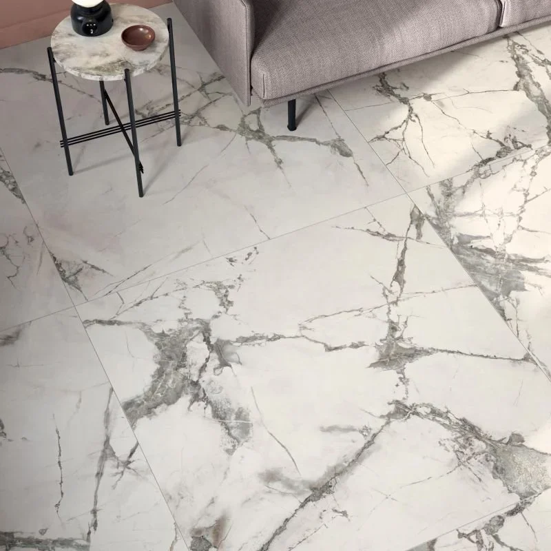 Boden mit weißen Marmorfliesen mit grauen und schwarzen Adern, Wohnzimmer mit einem kleinen Beistelltisch aus Marmor mit schwarzen Beinen und dekorativen Gegenständen, und einem grauen Sofa.