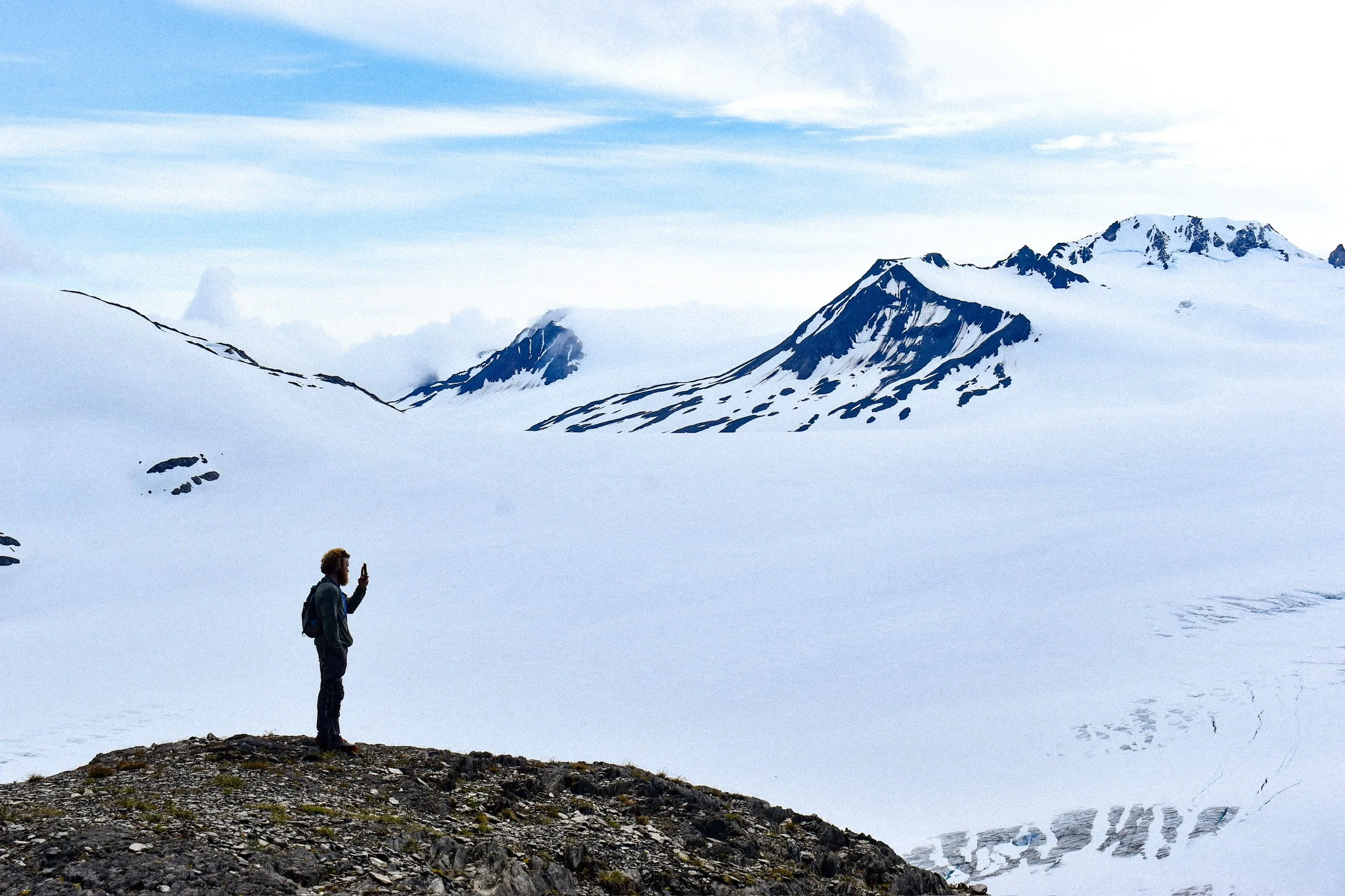 silhouette of a man taking a photo of a snowfield and mountain peaks
