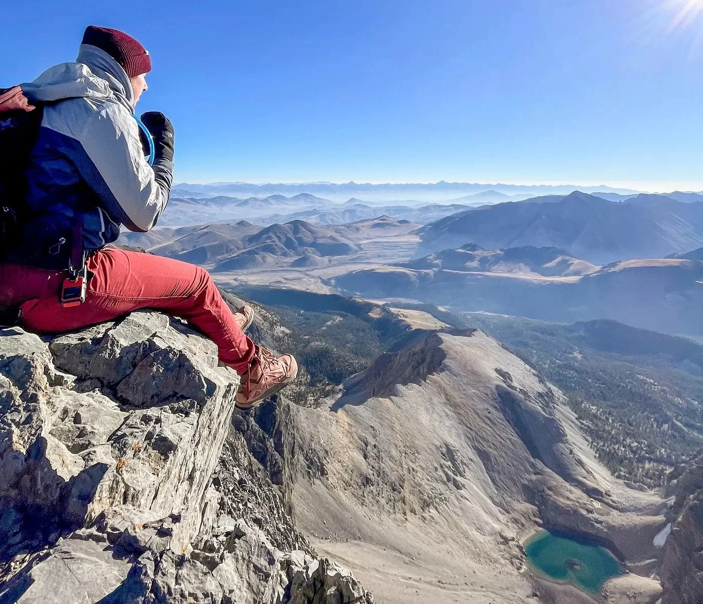A hiker sitting on a rocky ledge overlooking the view from Mount Borah, Idaho.
