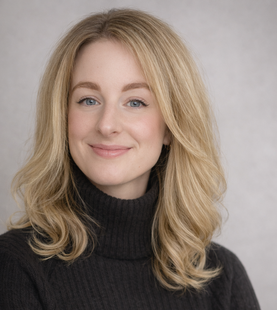 Porträt einer jungen Frau mit blondem, lockigem Haar, blauen Augen und einem schwarzen Rollkragenpullover, vor hellem Hintergrund.