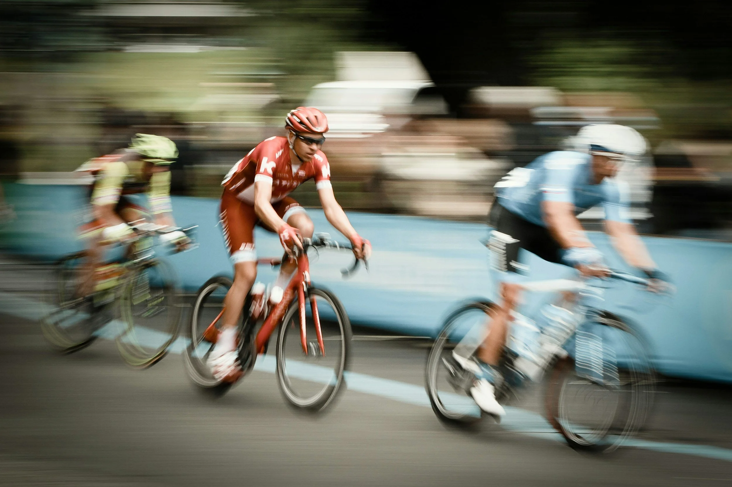 Drei Radfahrer in Bewegung unter Wettkampfdruck, mit verschwommenem Hintergrund, in einer sportlichen Fahrradszene.