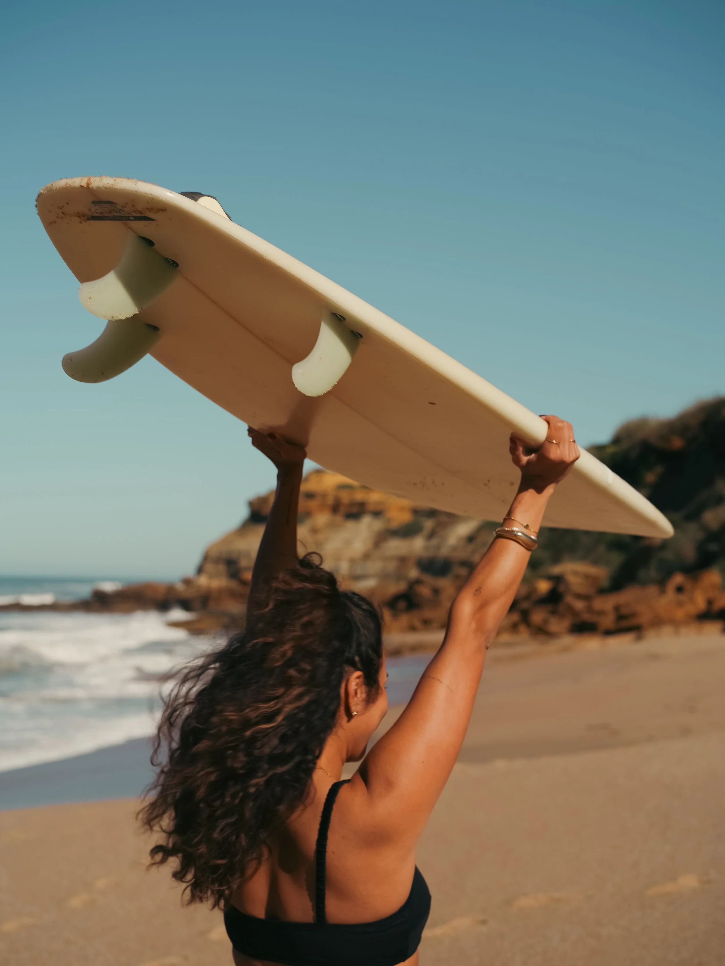 A woman holding a surfboard over her head while standing on the beach with free time during retreat experience