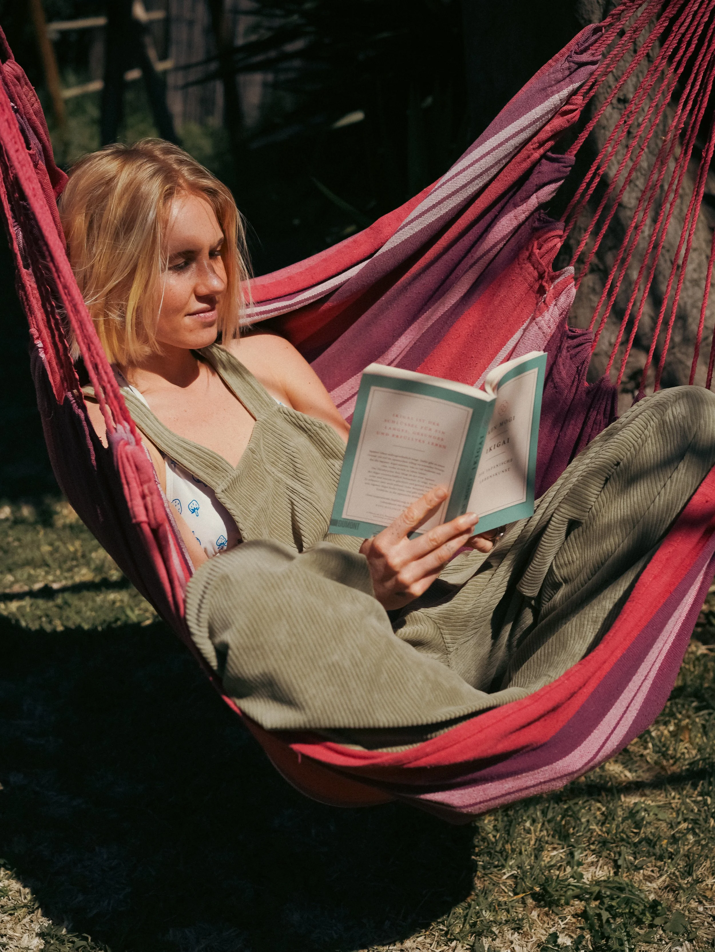 Women relaxing at retreat accommodation reading a book in a striped hammock outdoors.