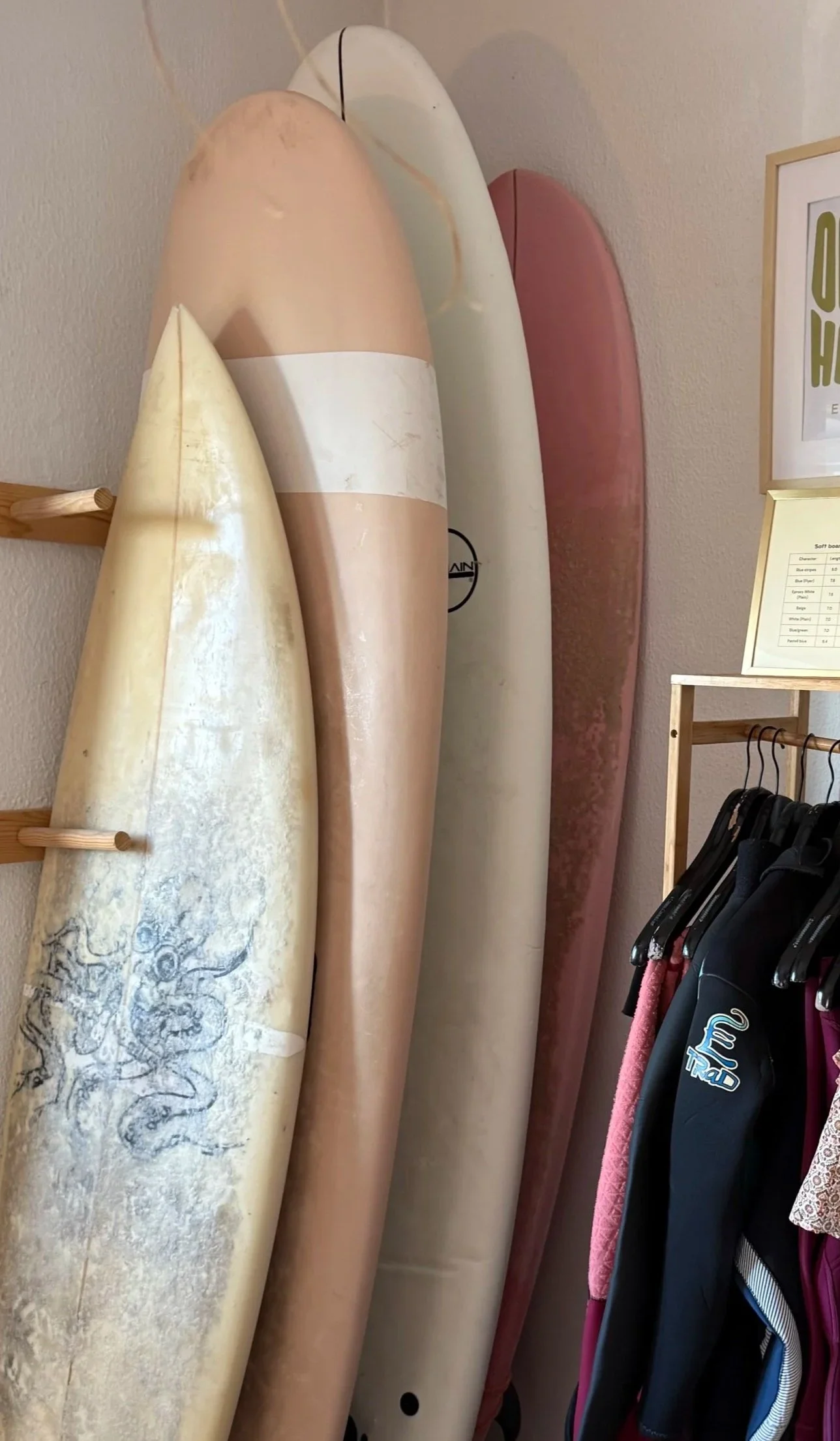 Four surfboards leaning against a wall with clothes hanging on a nearby rack for surf and yoga retreat in Portugal.