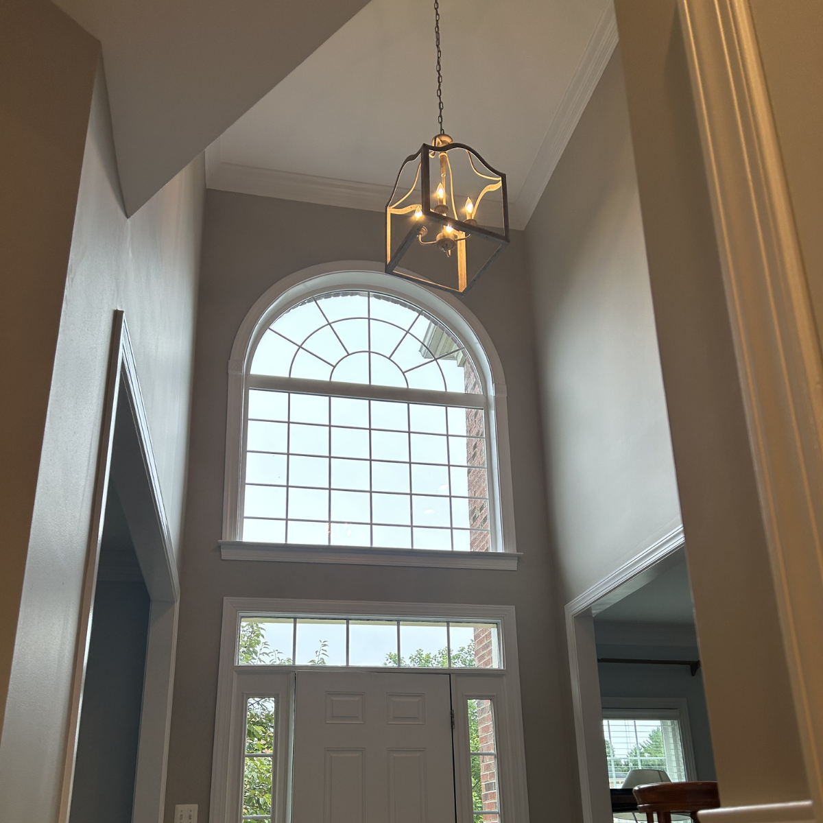 Interior view of a house entryway with a large arched window above the front door and a decorative hanging light fixture.