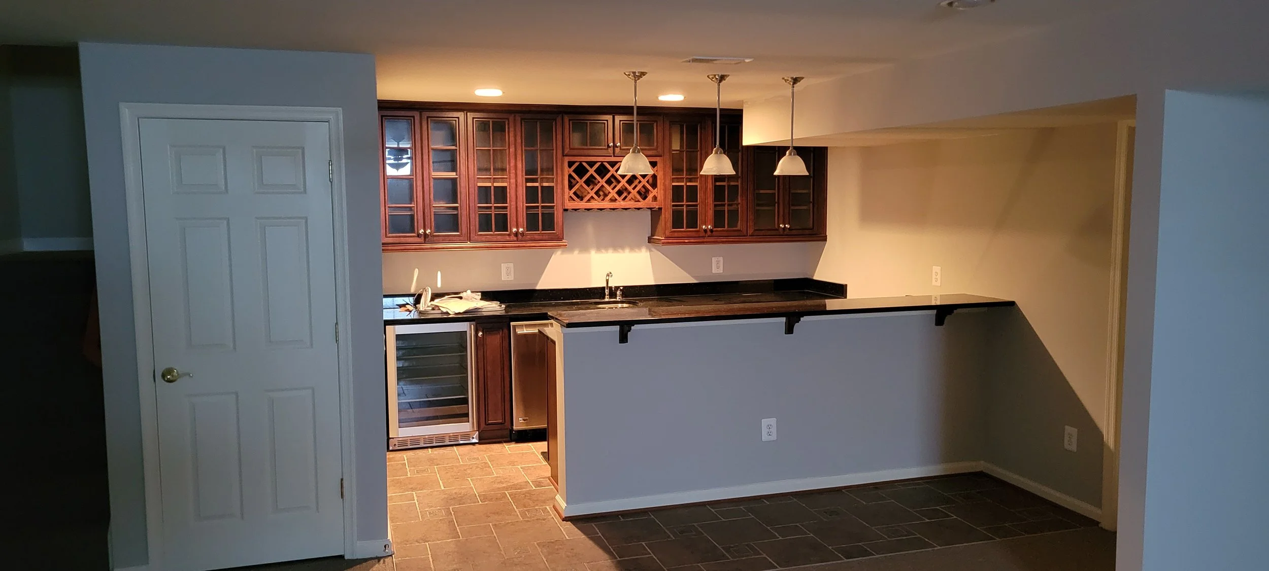 Winchester interior house painters CMT Painting Co. Kitchen area with dark wood cabinets, a black granite countertop, hanging pendant lights, a small wine rack, and a built-in mini fridge under the counter.