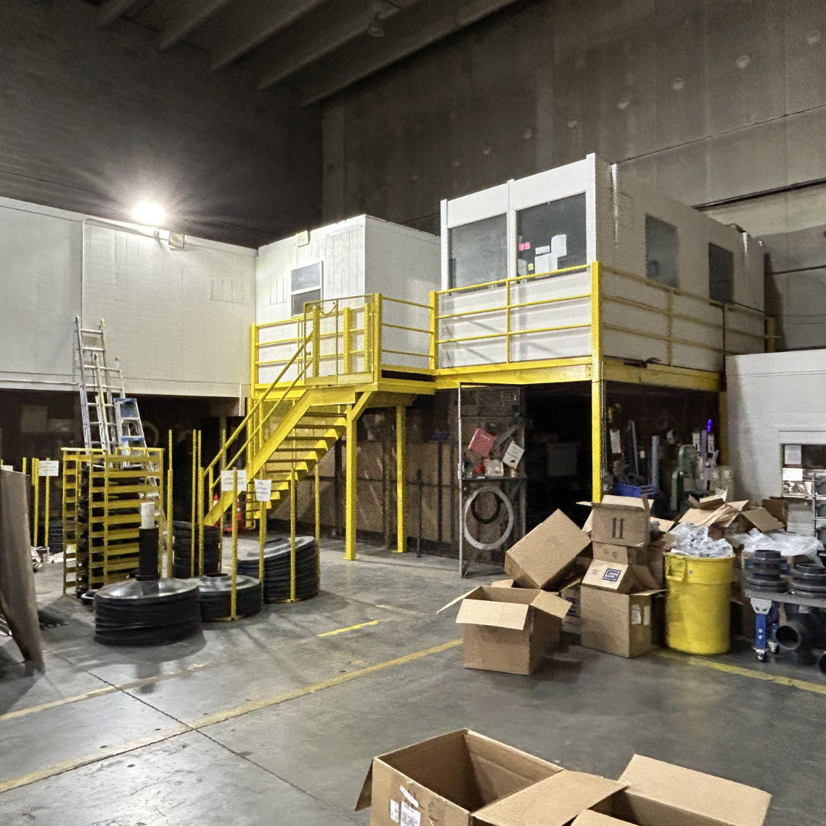 Commercial painting services Winchester Virginia Storage area with metal stairs leading up to a small enclosed office space with a yellow safety railing. The area has boxes, pallets, and various office and industrial supplies scattered around.