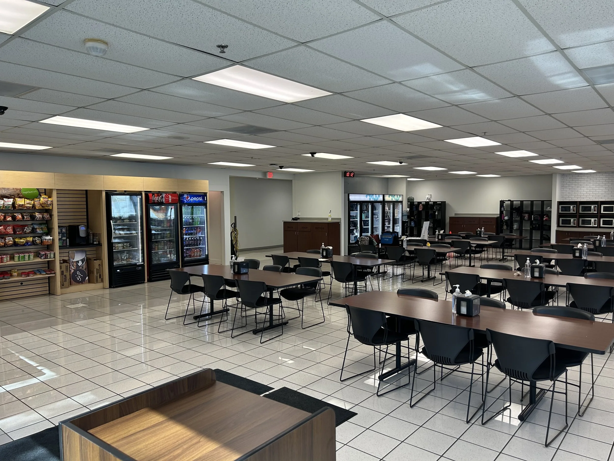 Empty cafe or cafeteria with black tables and chairs, vending machines, snacks, and a small counter in the background. CMT Painting Co. commercial painting Northern Virginia –