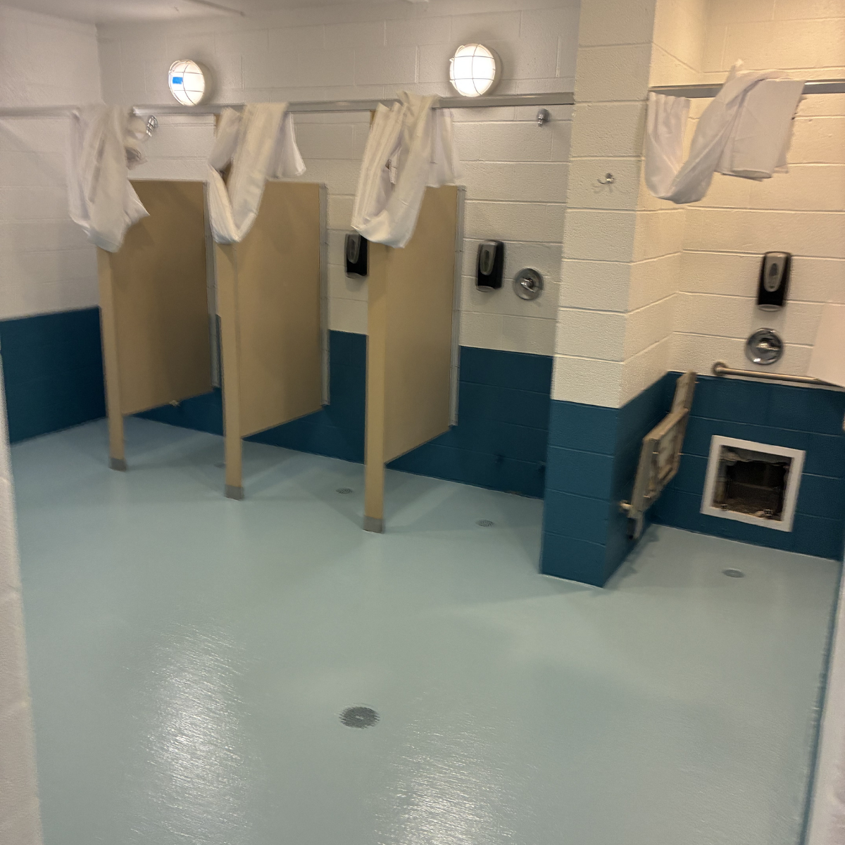 CMT Painting Co. commercial painters Winchester VA  Public restroom with three private stalls and white urinals, towels hanging from a rack, and a blue and white tiled wall.