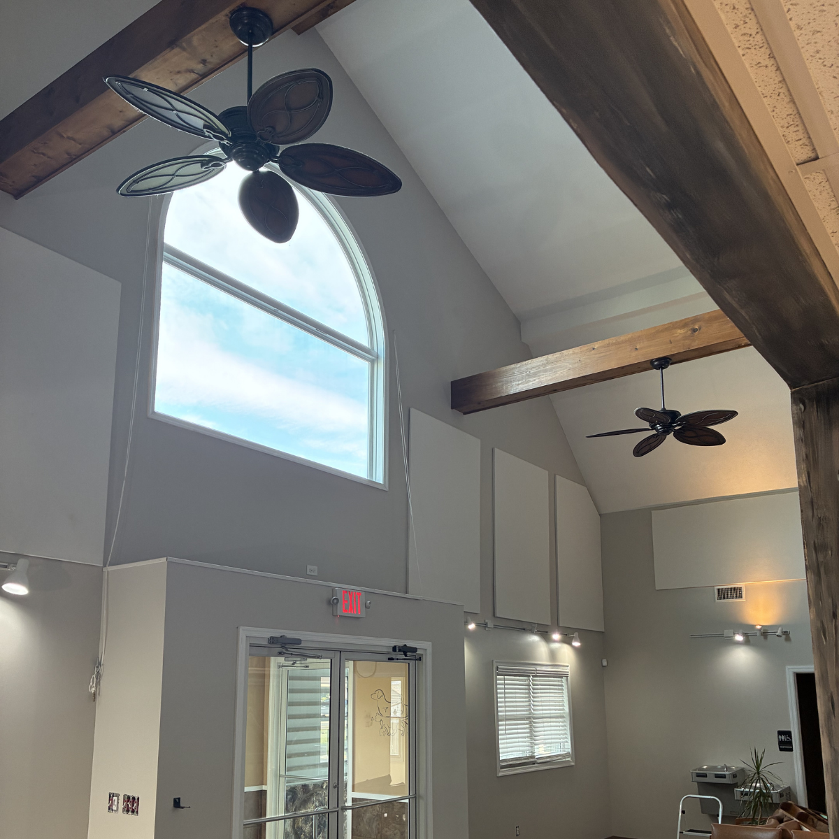 Winchester commercial painters CMT Painting Co. Interior view of a room with high vaulted ceiling, large arched window, exposed wooden beams, ceiling fans with leaf-shaped blades, potted plant, and a glass door leading outside.