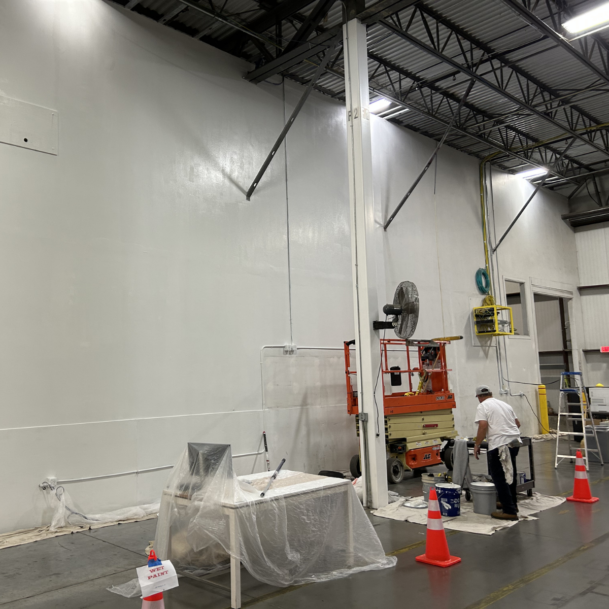 Commercial painting services Winchester Virginia - Worker painting a high wall inside a warehouse with safety cones and equipment around.