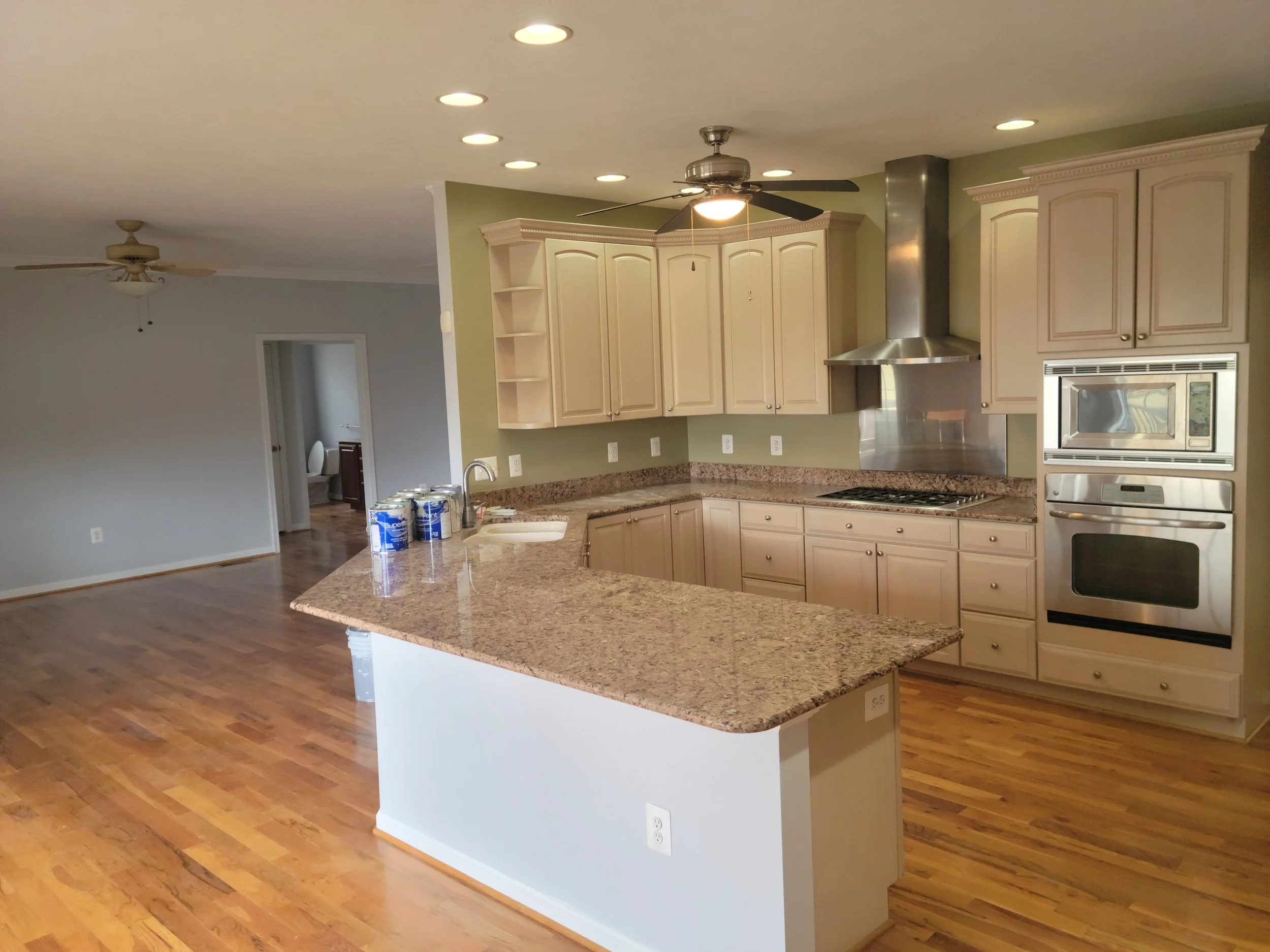 CMT Painting Co. interior home painters Northern Virginia Empty kitchen with granite countertops, light wood cabinetry, stainless steel appliances, hardwood floors, green accent wall, and ceiling fans.