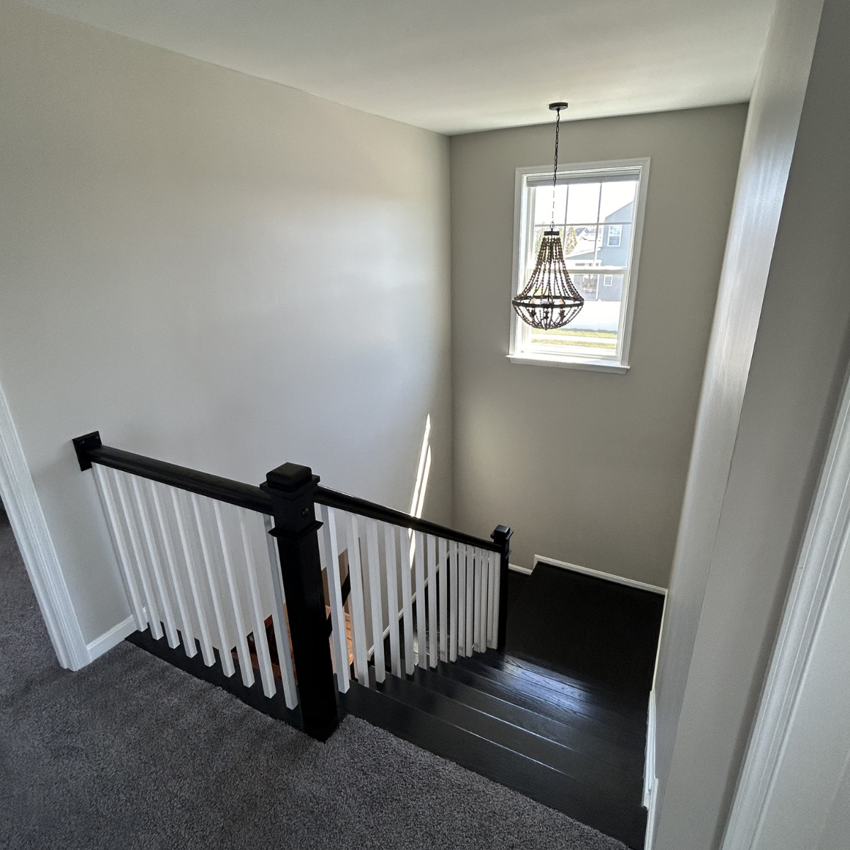 View of a staircase landing with a white railing, a window with natural daylight, and a decorative hanging chandelier in a modern, bright home interior