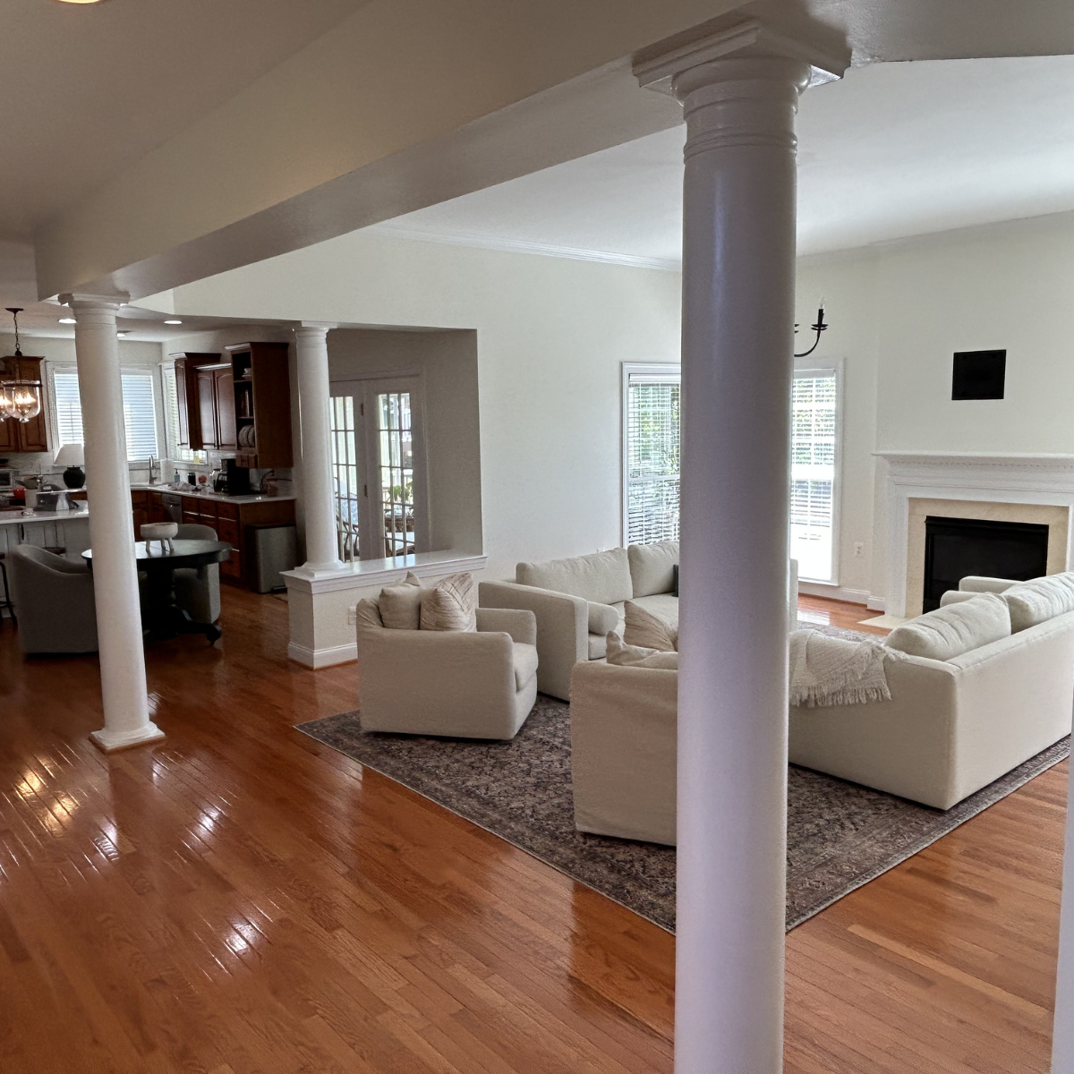 Living room with white sofas, wooden flooring, large windows, fireplace, and columns.