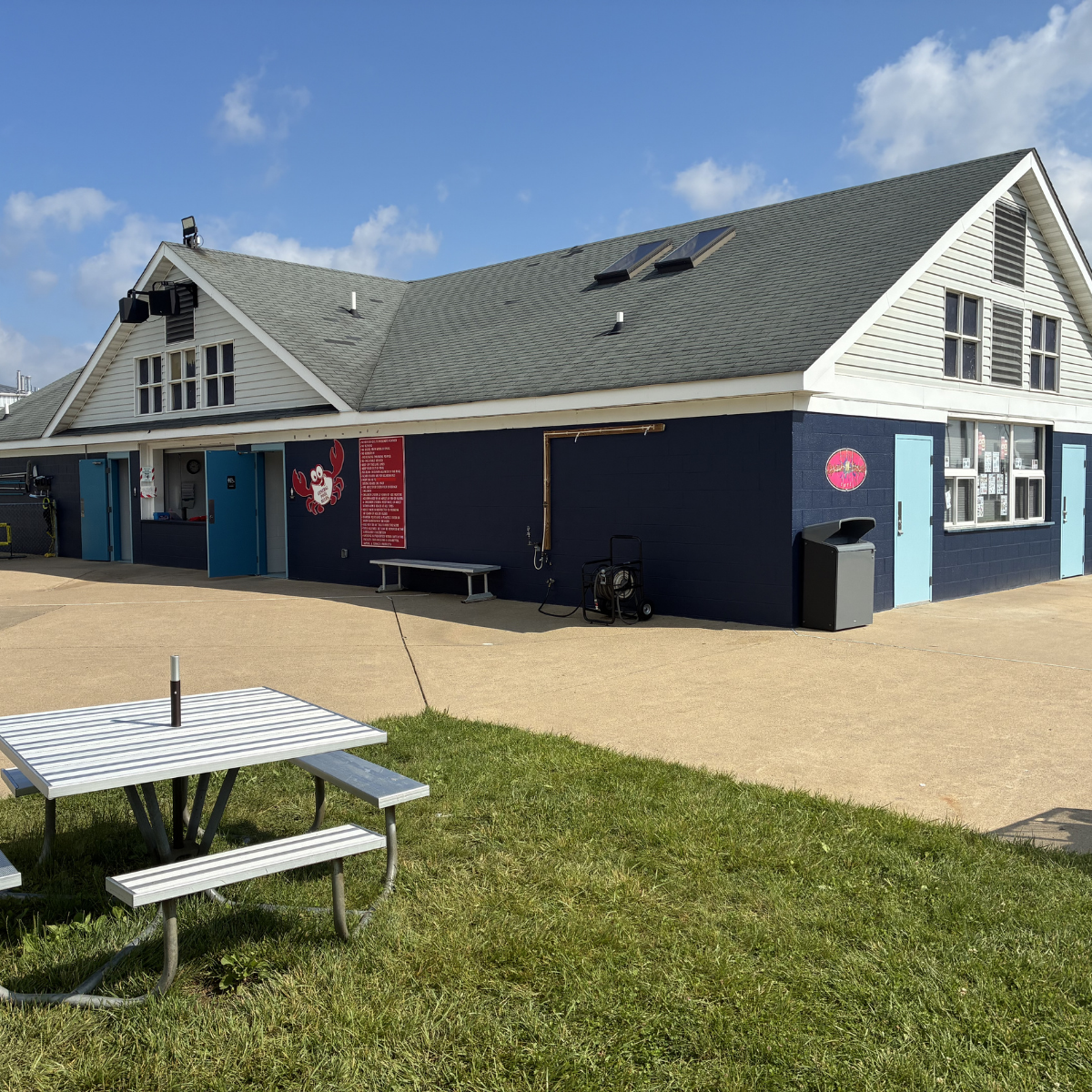 Commercial painters Winchester Virginia – Building with a white gabled roof, blue siding, and decorative crab and menu signs, with a picnic table in front and a concrete patio area, under a partly cloudy sky.
