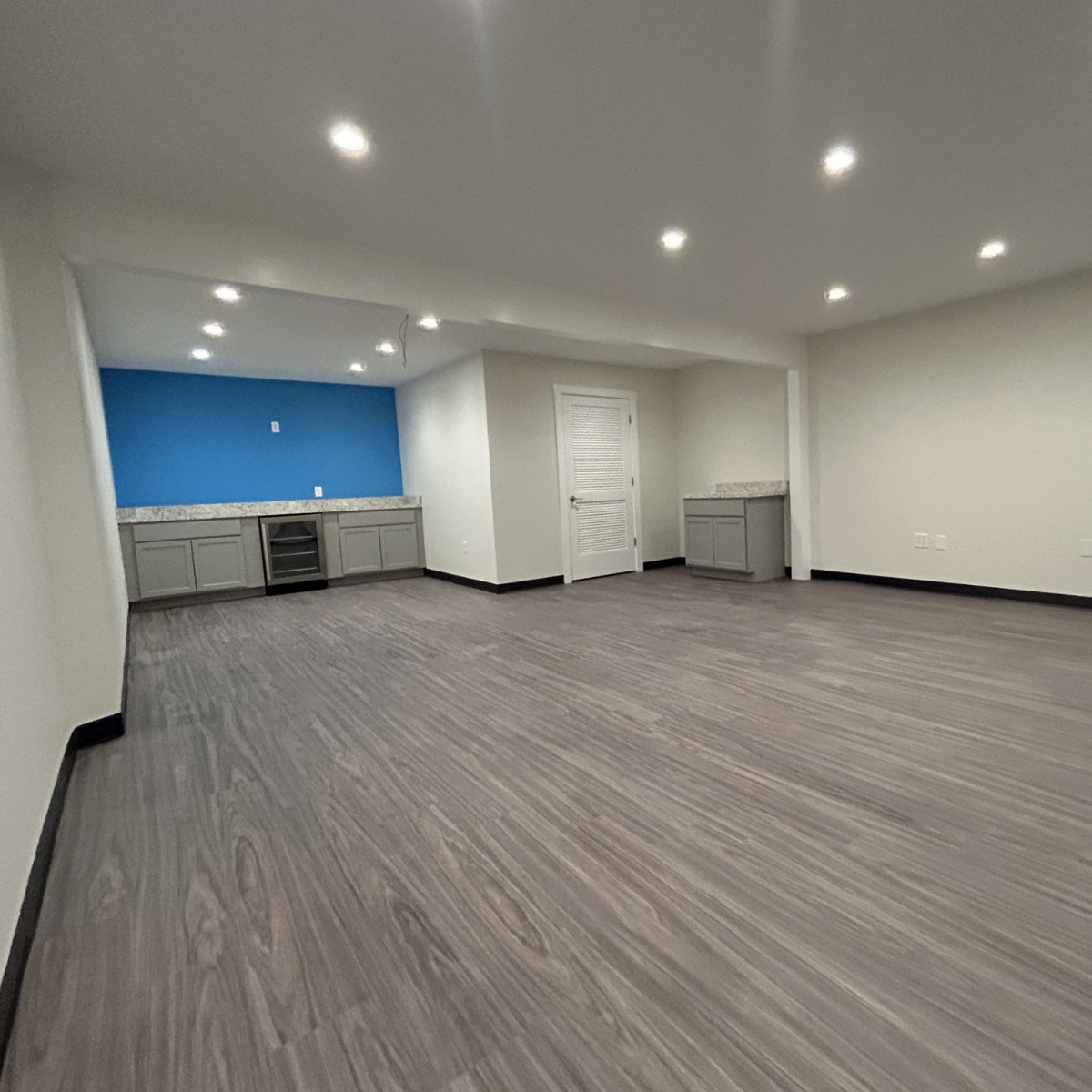 Commercial painting services Winchester Virginia  Unfurnished open room with wood-look flooring, white walls, ceiling lights, gray cabinets, blue accent wall, and a white door.