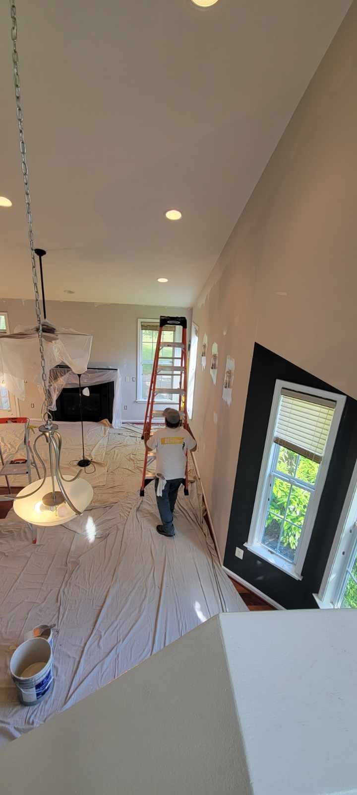 CMT Painting Co. interior home painters Northern Virginia A person working on home renovation, standing on a ladder in a living room with construction materials, covered furniture, and painter's supplies.