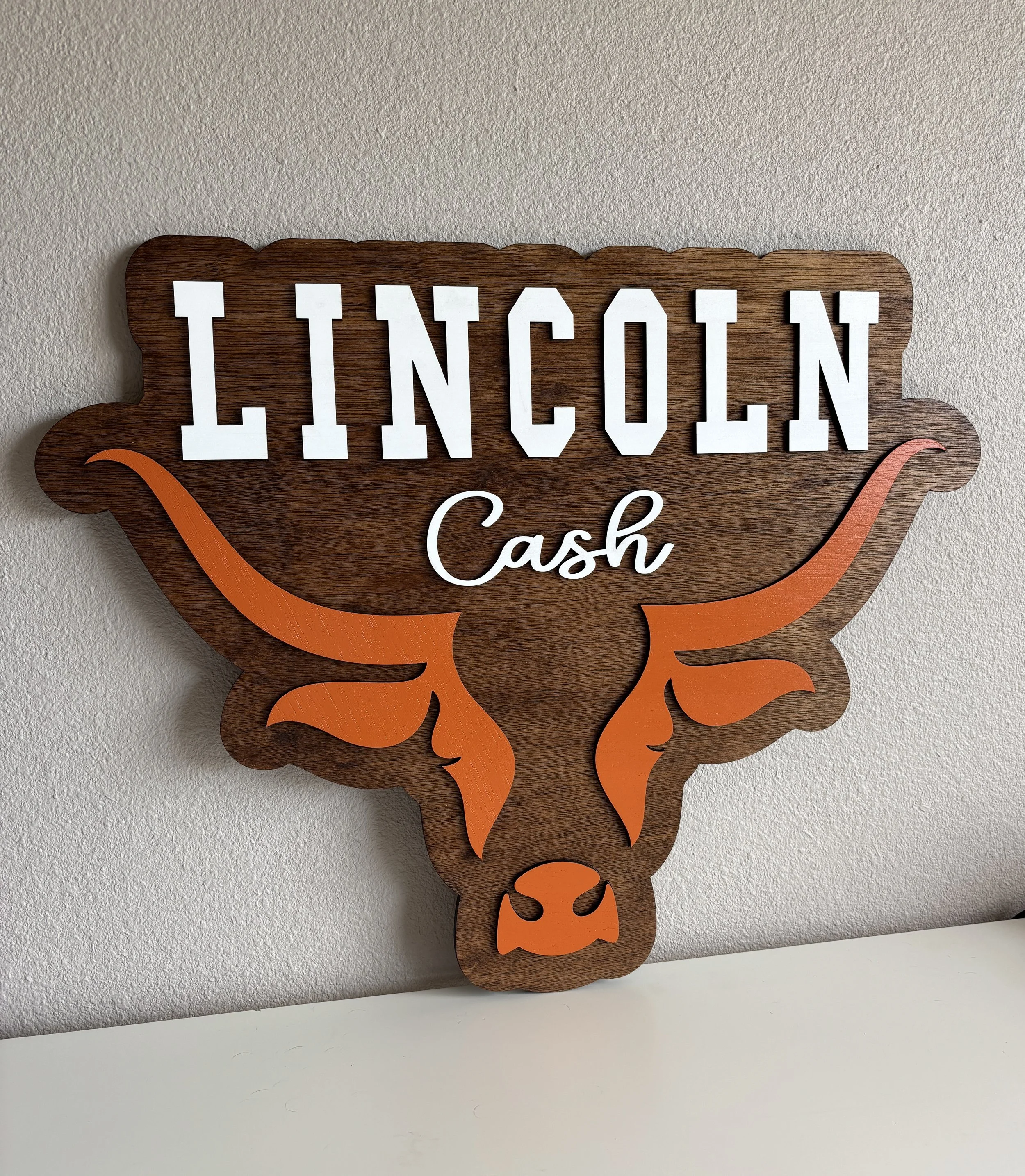 A wooden sign with the words "Lincoln Cash" and a stylized illustration of a longhorn steer in orange.