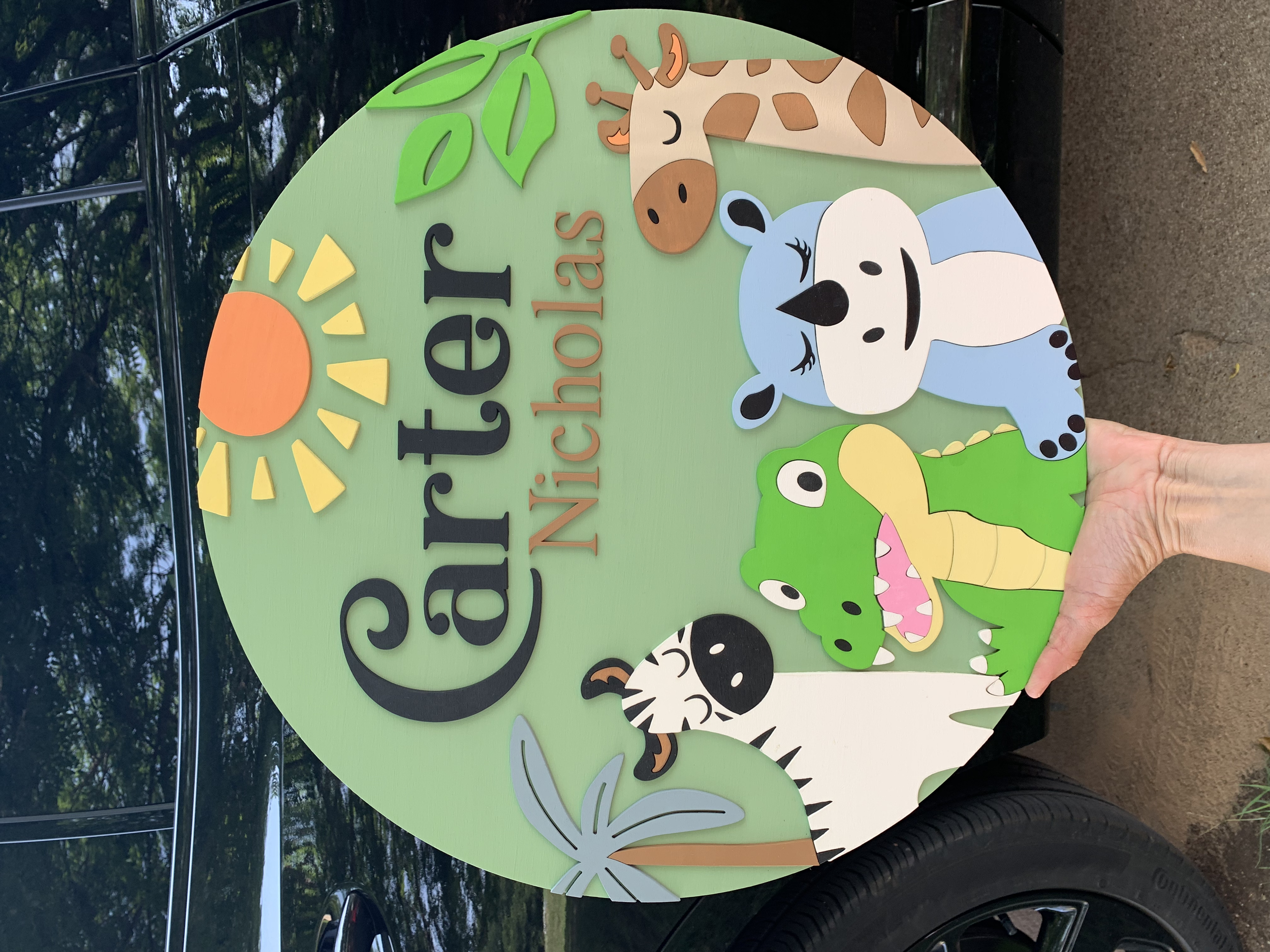 Colorful sign with illustrations of cartoon animals including a giraffe, zebra, crocodile, alligator, and a koala bear, with the text "Garden of Nicheolas" and a sun graphic.