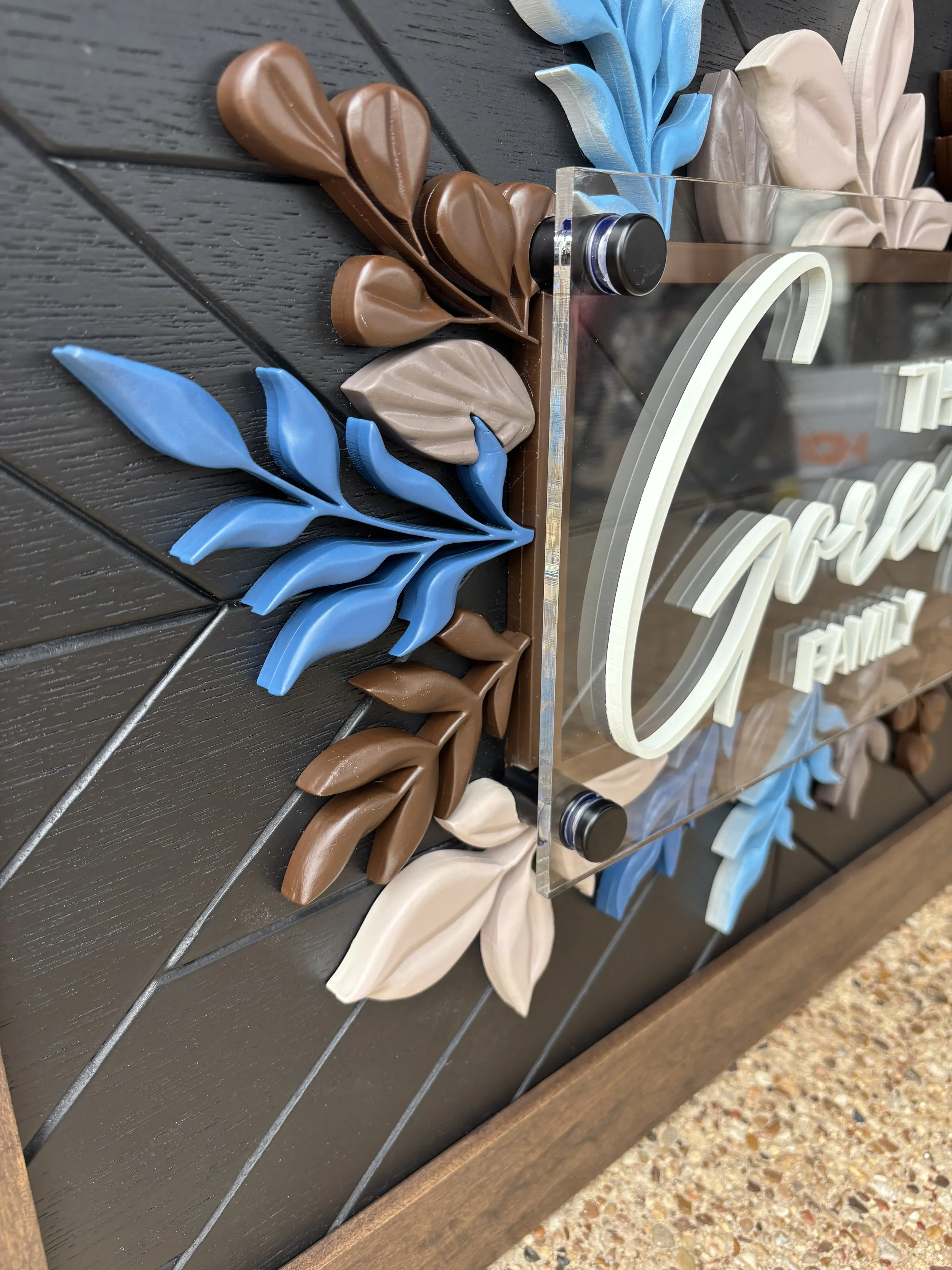 Decorative photo frame with a clear acrylic panel, surrounded by brown, blue, beige, and taupe leaves on a dark wooden background.
