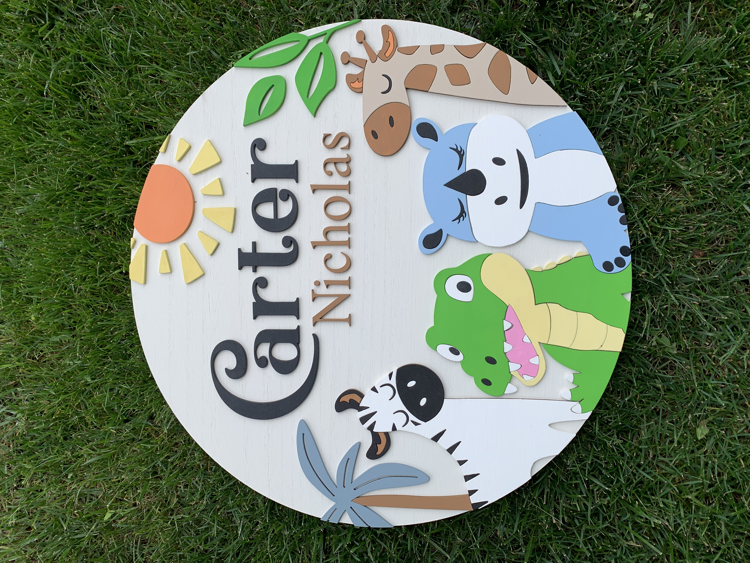 Decorative sign with the words 'Carter NICU NICU Babies' on a white background, featuring cartoon illustrations of a giraffe, blue bear, green crocodile, zebra, and palm tree, placed on grass.