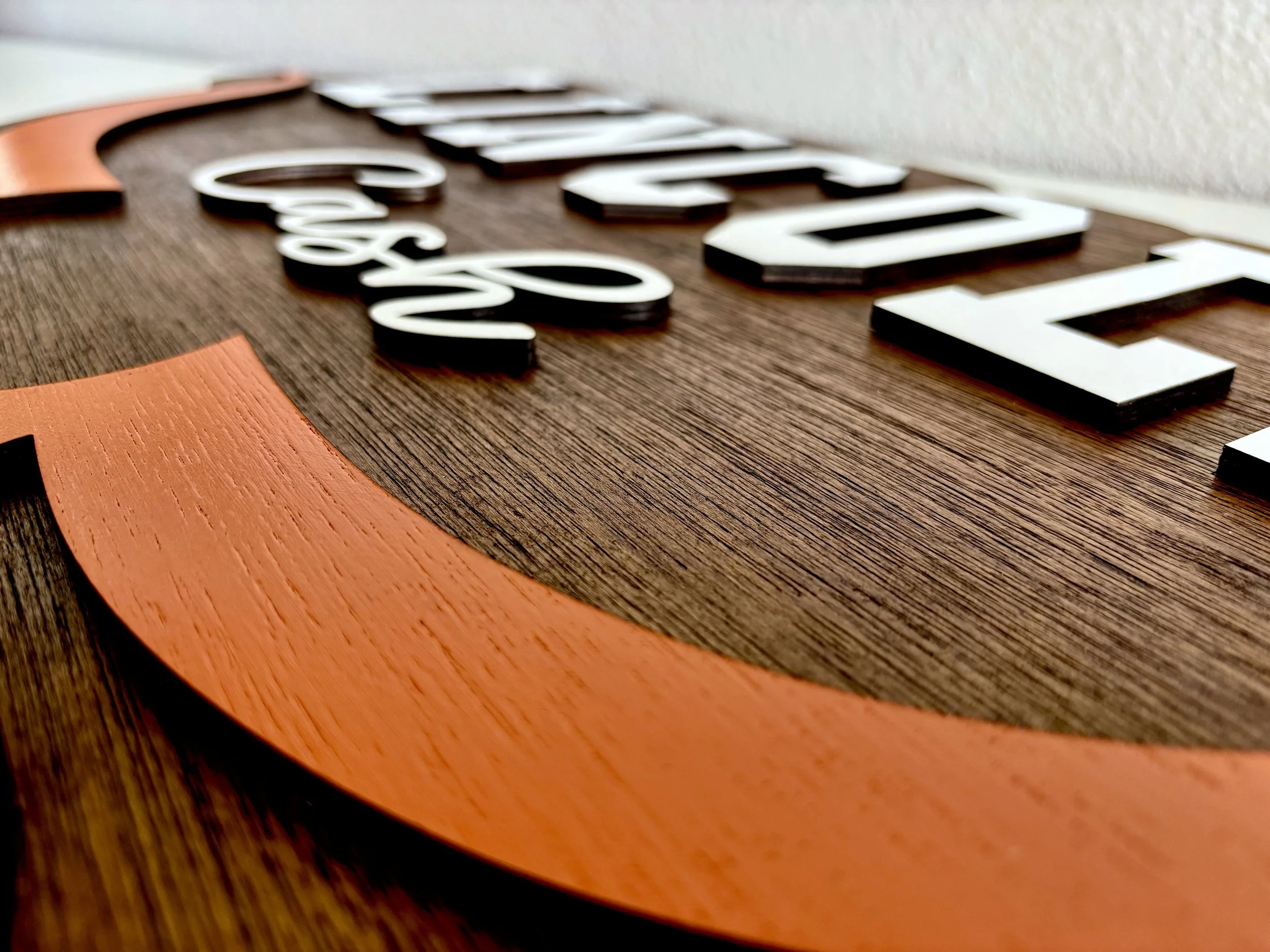 Close-up of a wooden wall decoration with white 3D letters spelling 'SABER' and an orange curved design on the left side.