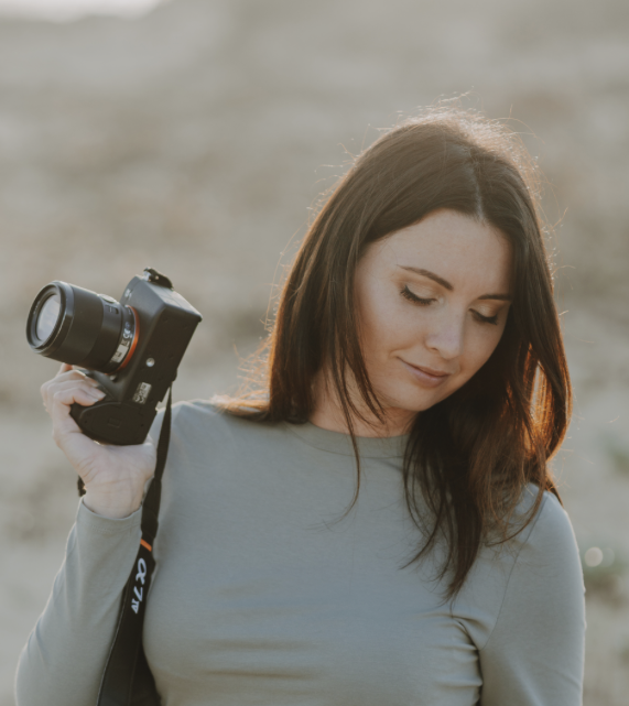 Femme avec appareil photo en plein air, souriante, lors d'une séance photo au coucher du soleil.