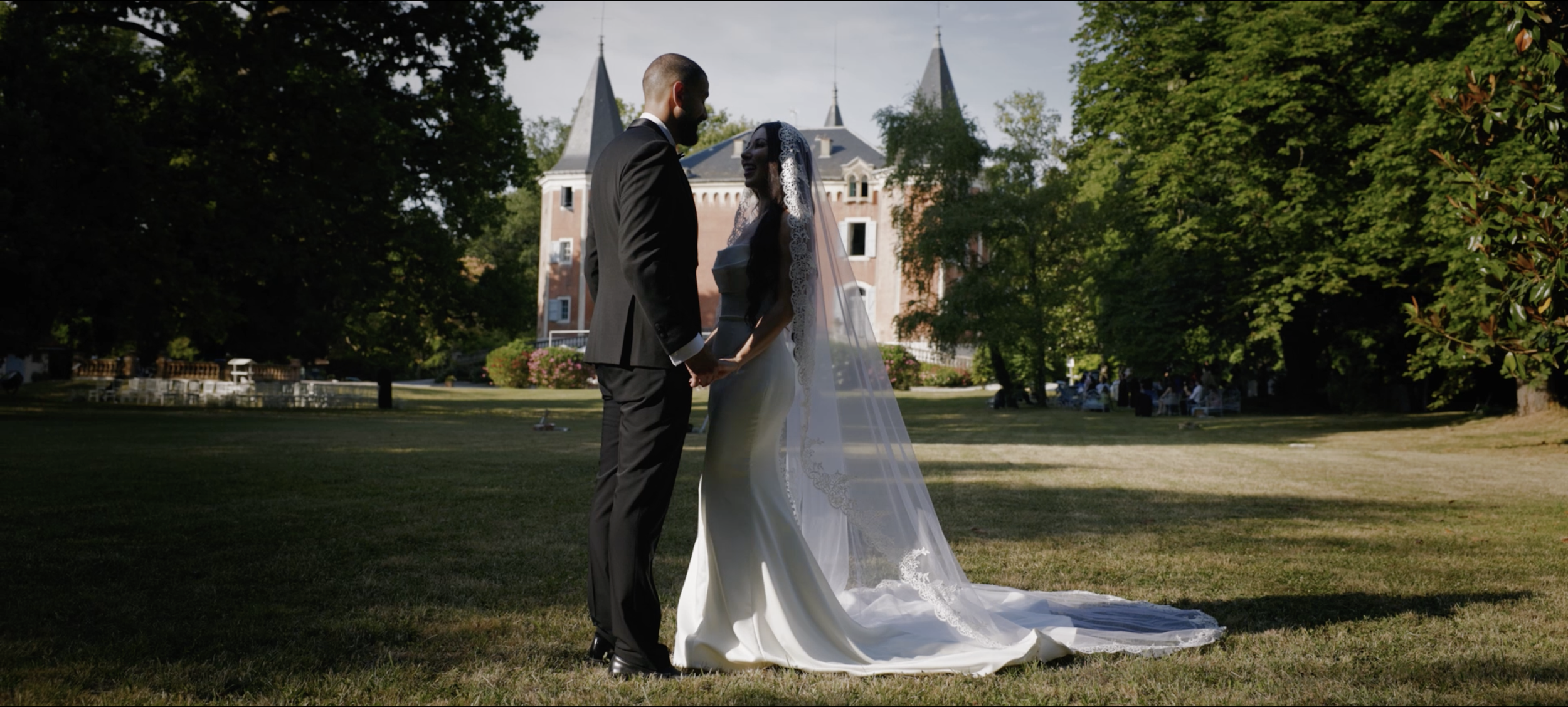 Un couple marié se tenant la main dans un parc, avec un château en arrière-plan, lors d'une cérémonie de mariage en plein air.