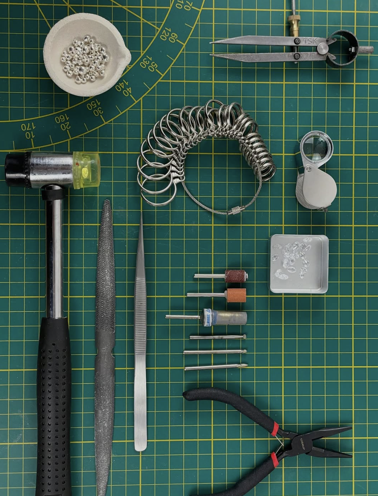 Outils de bijoux, comprenant une pince coupante, une pince à bec fin, une loupe, un cylindre en métal, et d'autres accessoires pour la création de bijoux en argent ou en or.